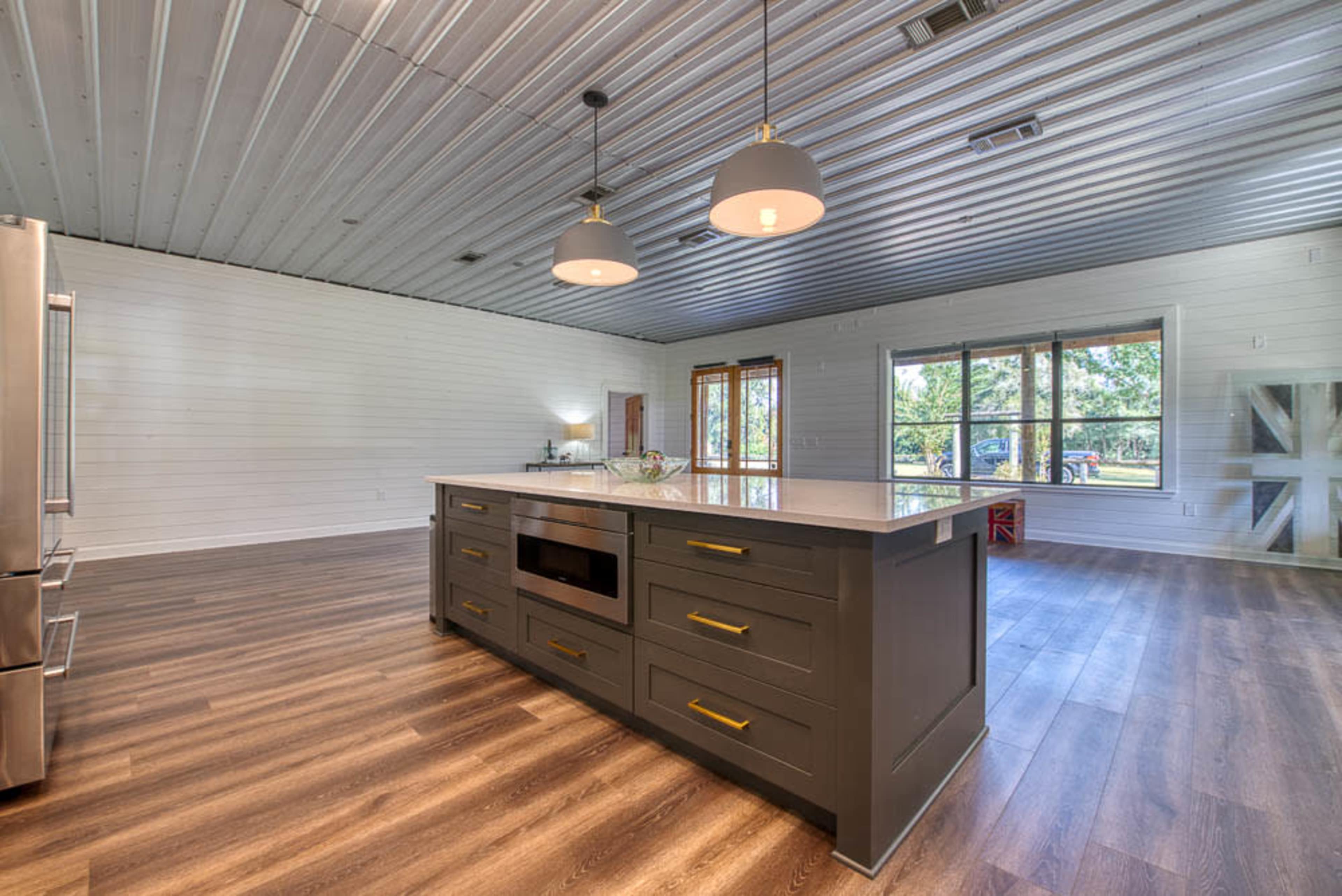 A modern kitchen with a central island, stainless steel appliances, and large windows offering a view of the outdoors.