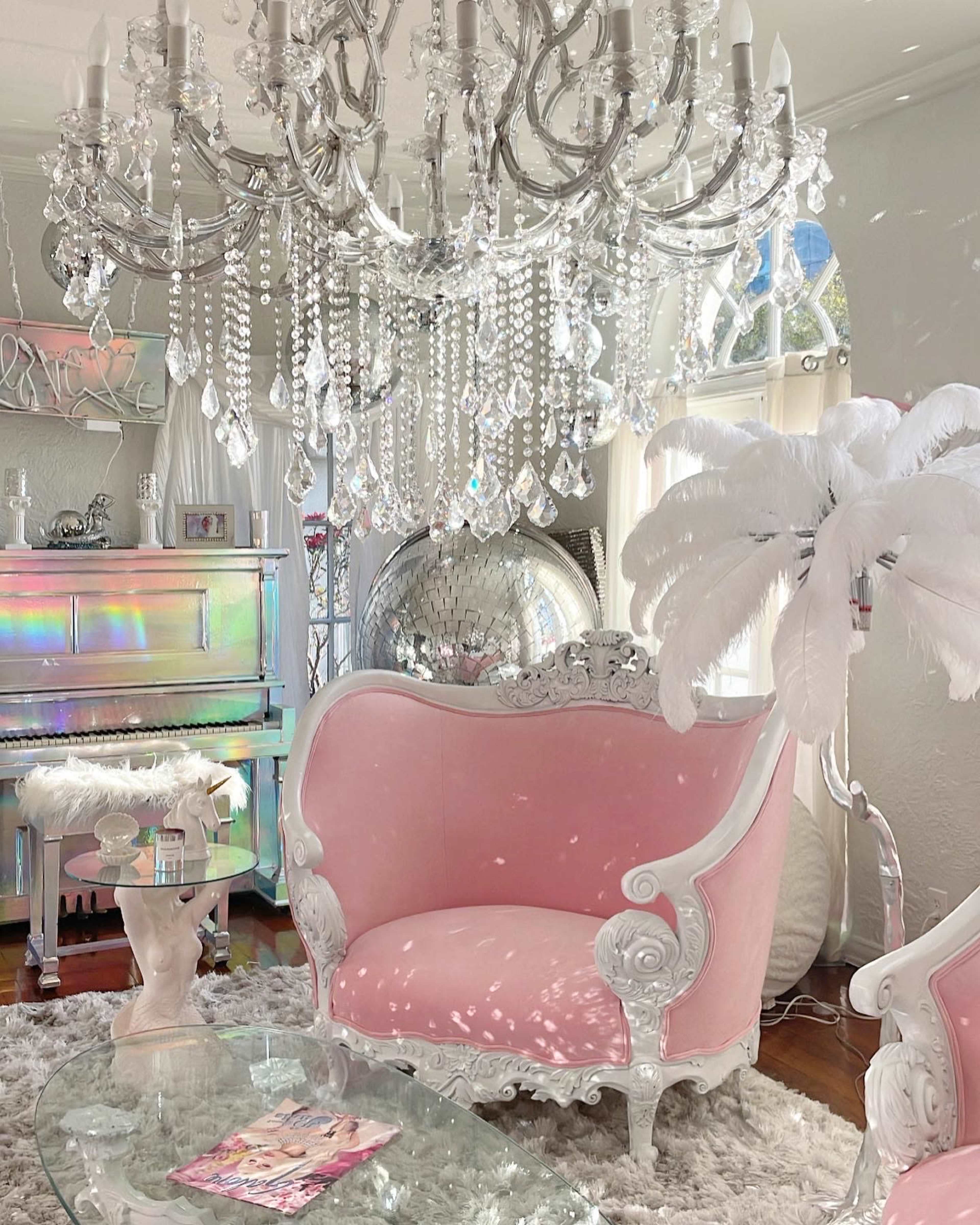 The room features a pink upholstered sofa, a crystal chandelier, and a mirrored disco ball, creating a bright and elegant ambiance.