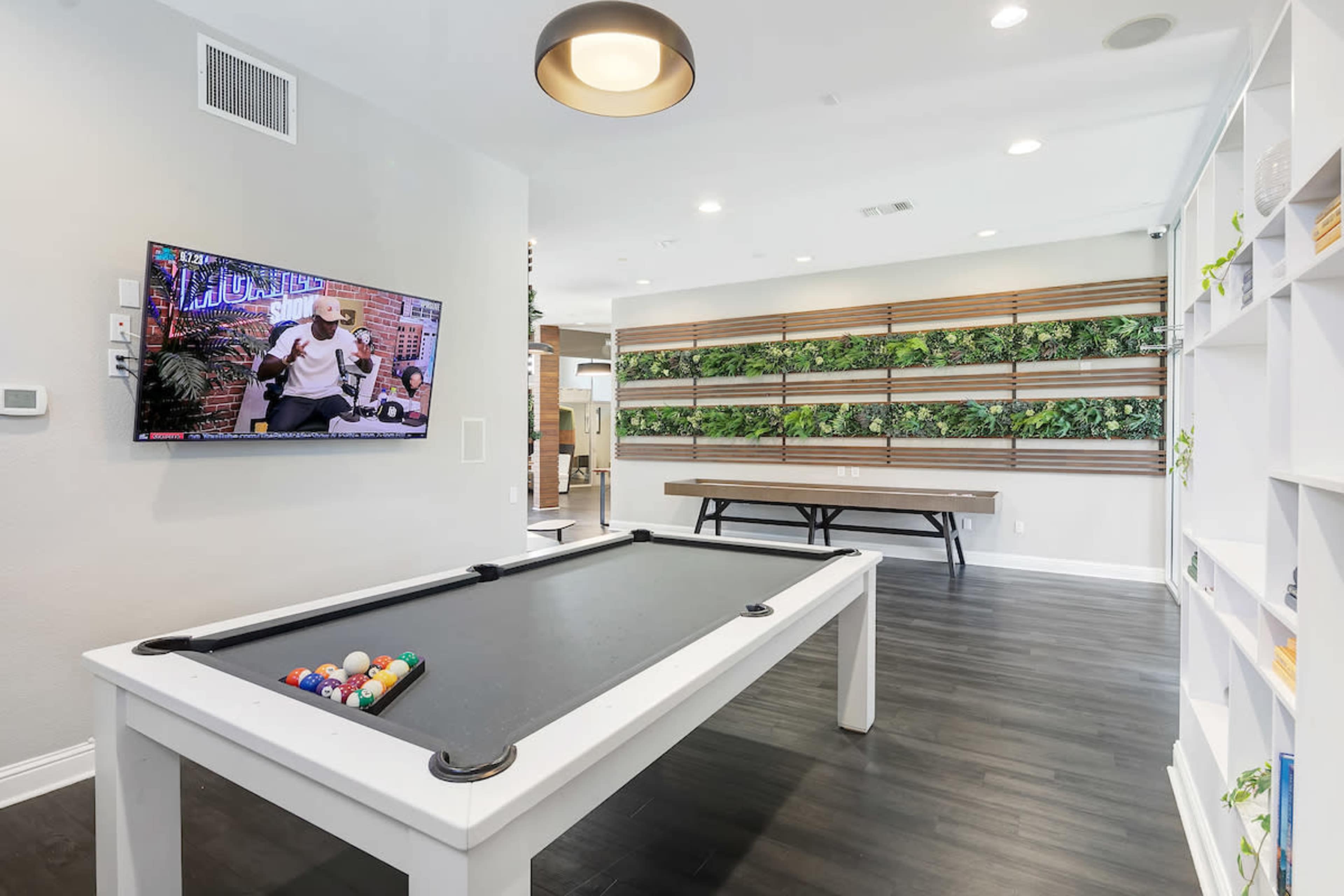 A modern game room with a pool table, a wall-mounted television, and a wooden table against a backdrop of vertical greenery.