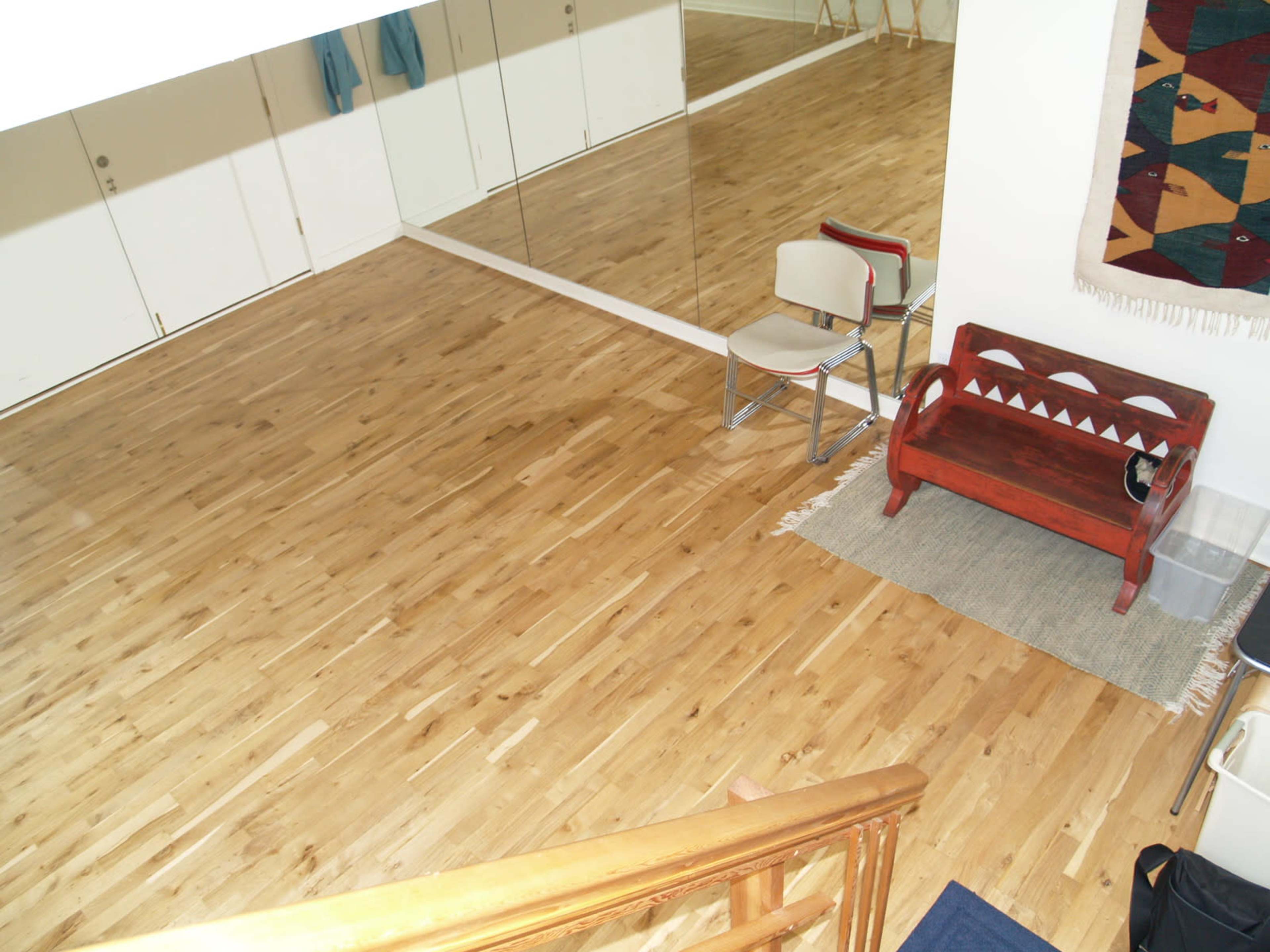 A wooden floor space with a chair, a red bench, and a large mirror reflecting the room.