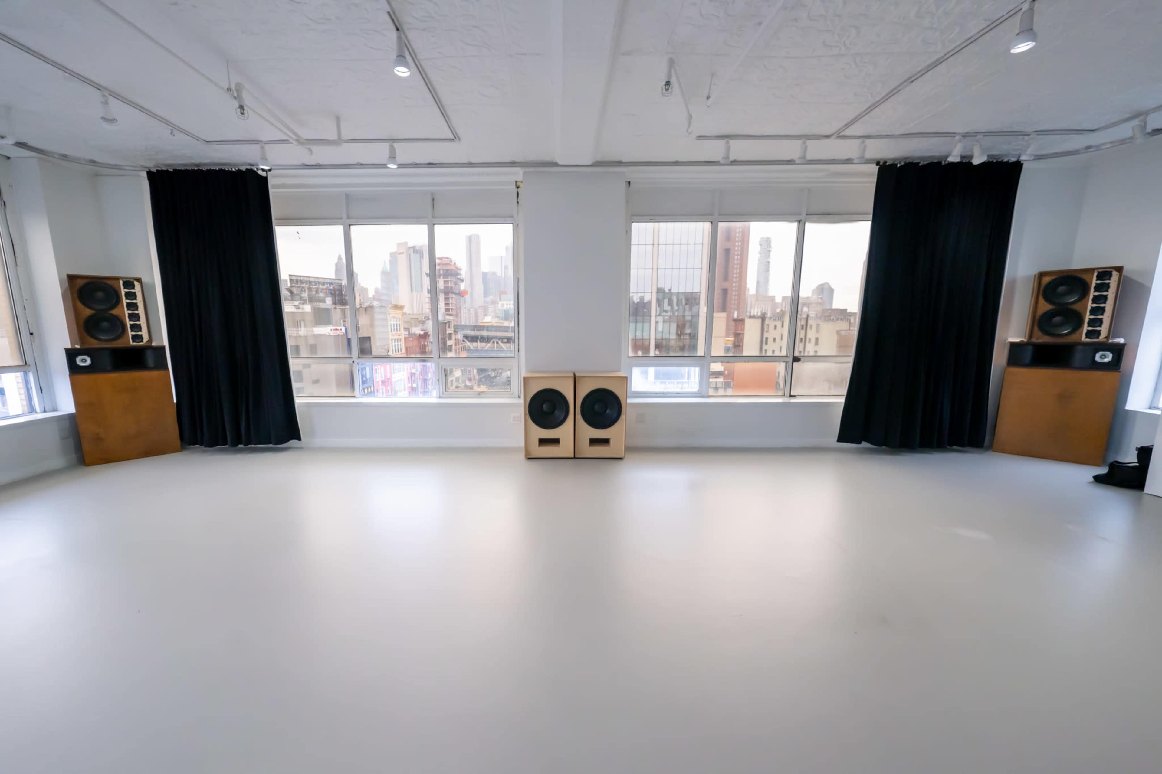 A spacious room with large windows, two tall speakers on either side, and a view of a city skyline outside.