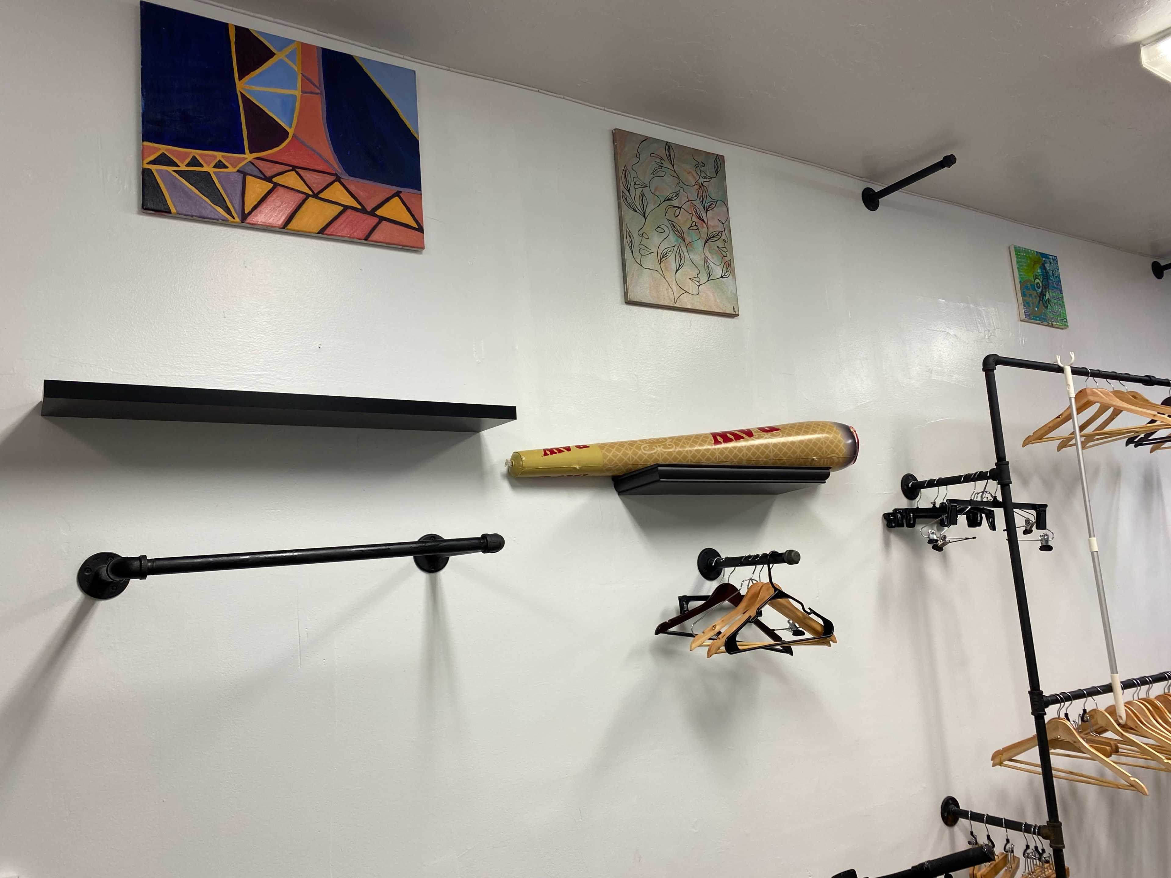 A wall with two shelves and several hangers, adorned with colorful artwork above.