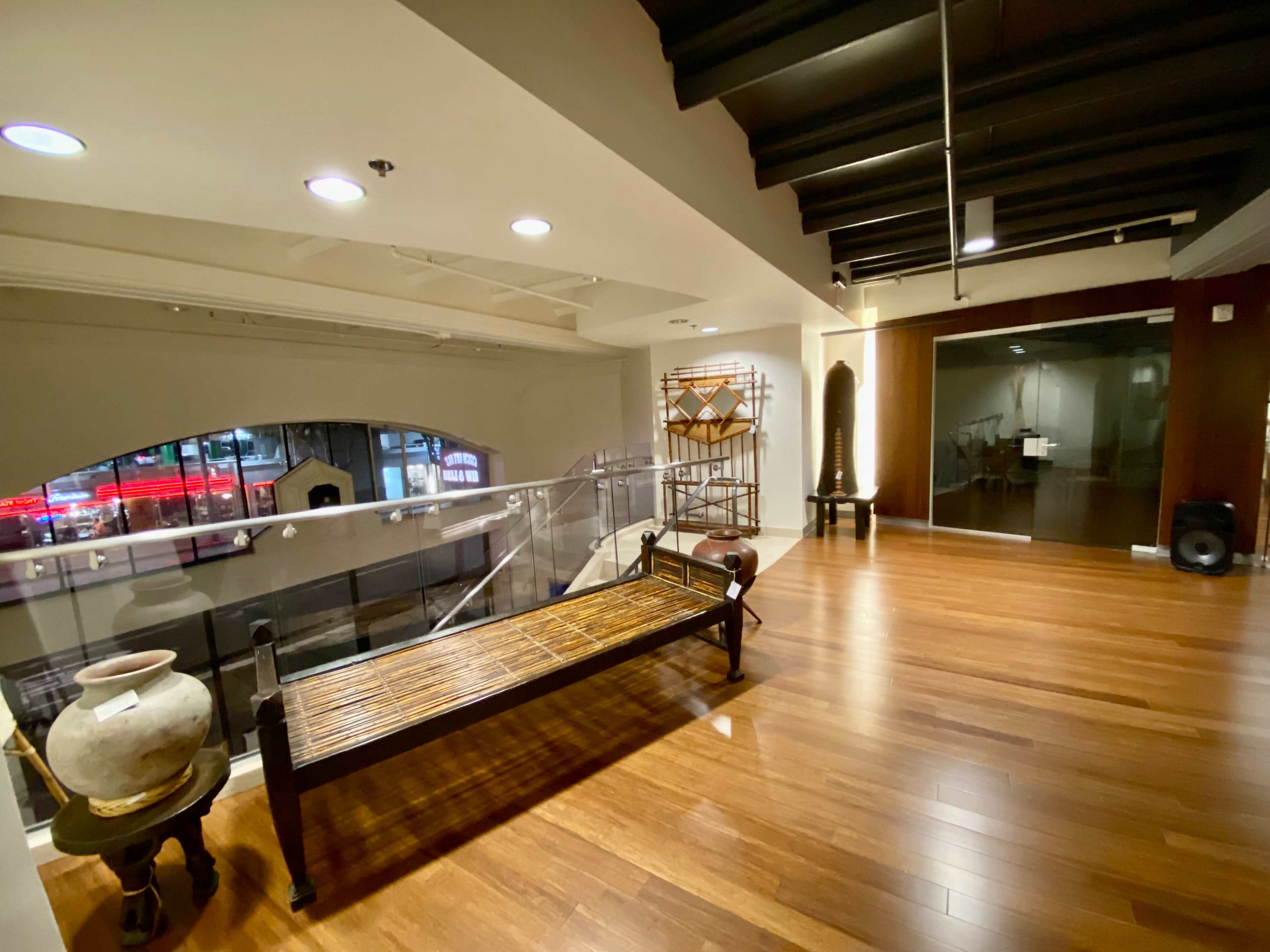 The image shows a modern interior space with wooden floors, a decorative bench, and various art pieces displayed on shelves.