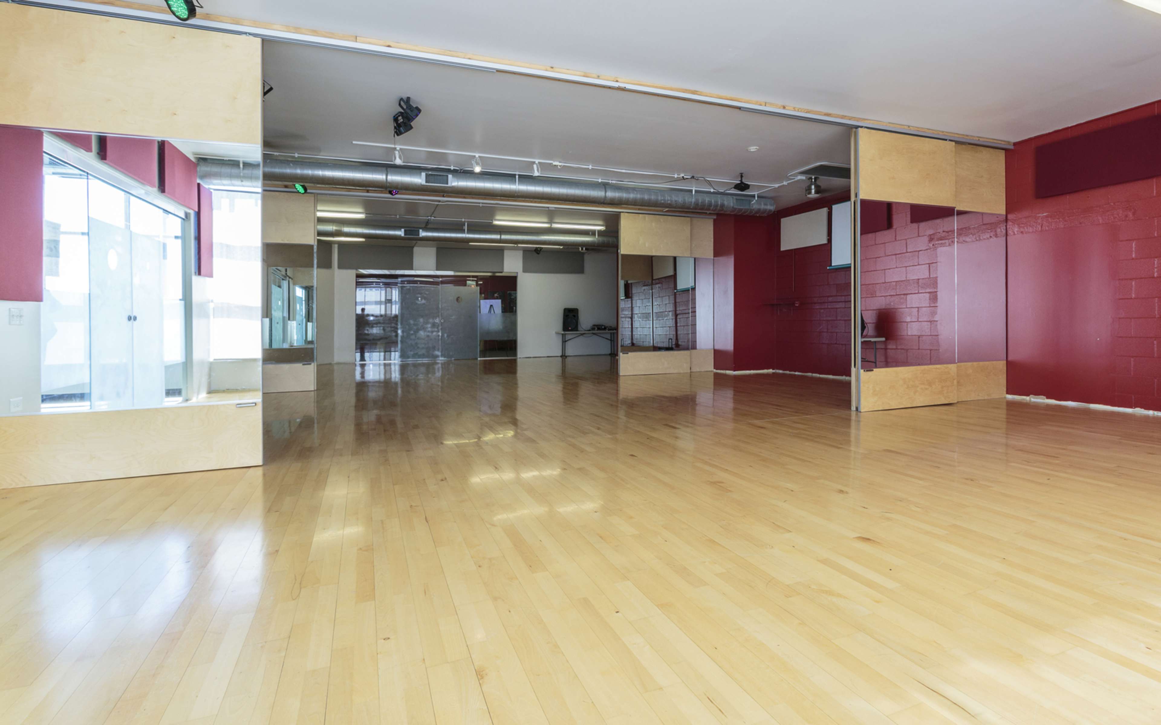 A spacious dance studio with wooden flooring, mirrored walls, and red accent walls.