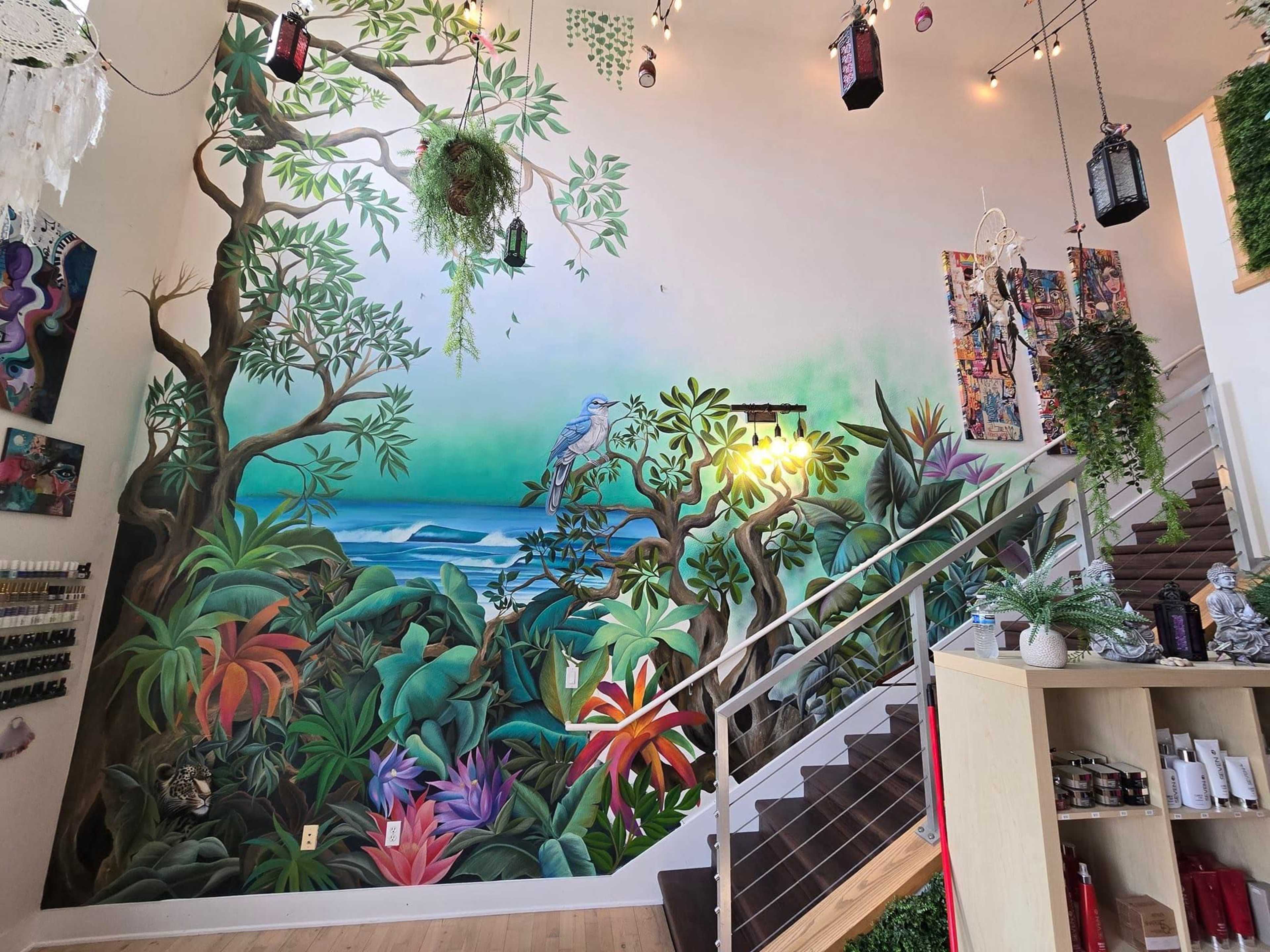 A vibrant mural depicting tropical plants and a bird, set against a backdrop of a blue ocean and green foliage, situated near a staircase in a well-lit space.