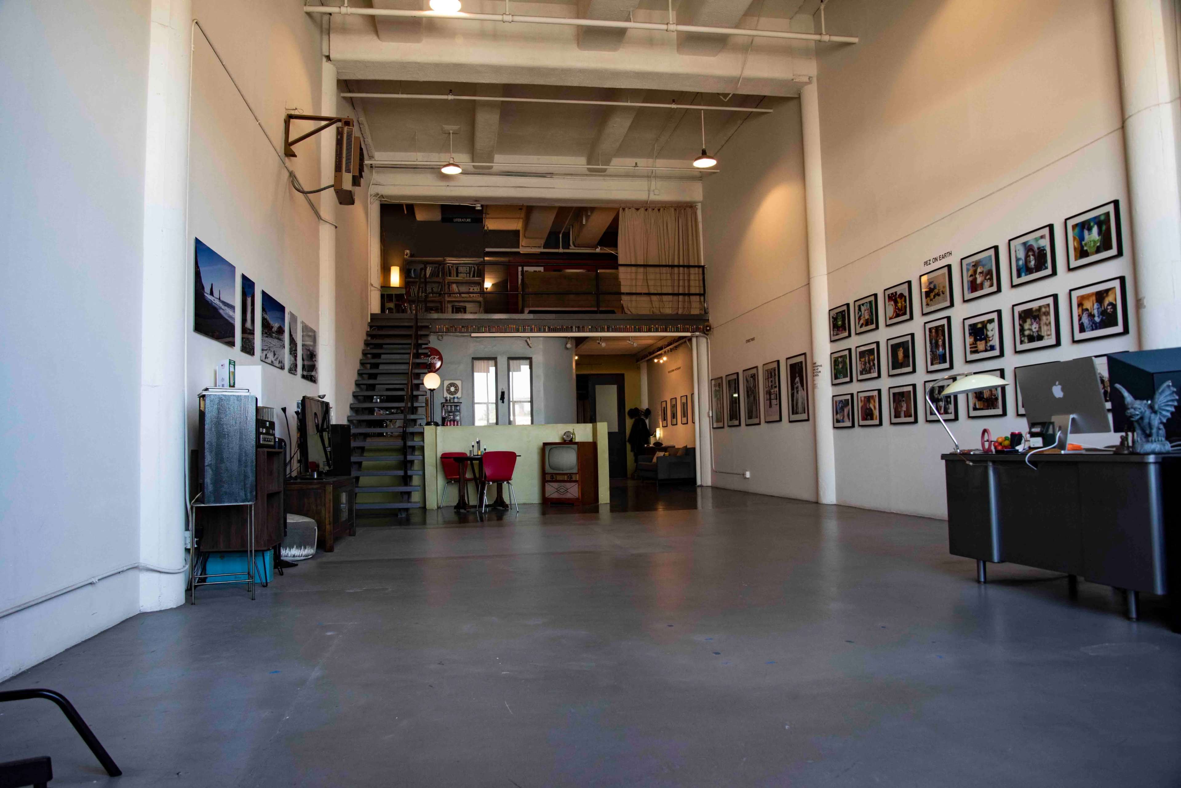 A spacious, modern studio with high ceilings, a staircase leading to an upper level, and framed photographs displayed on the walls.