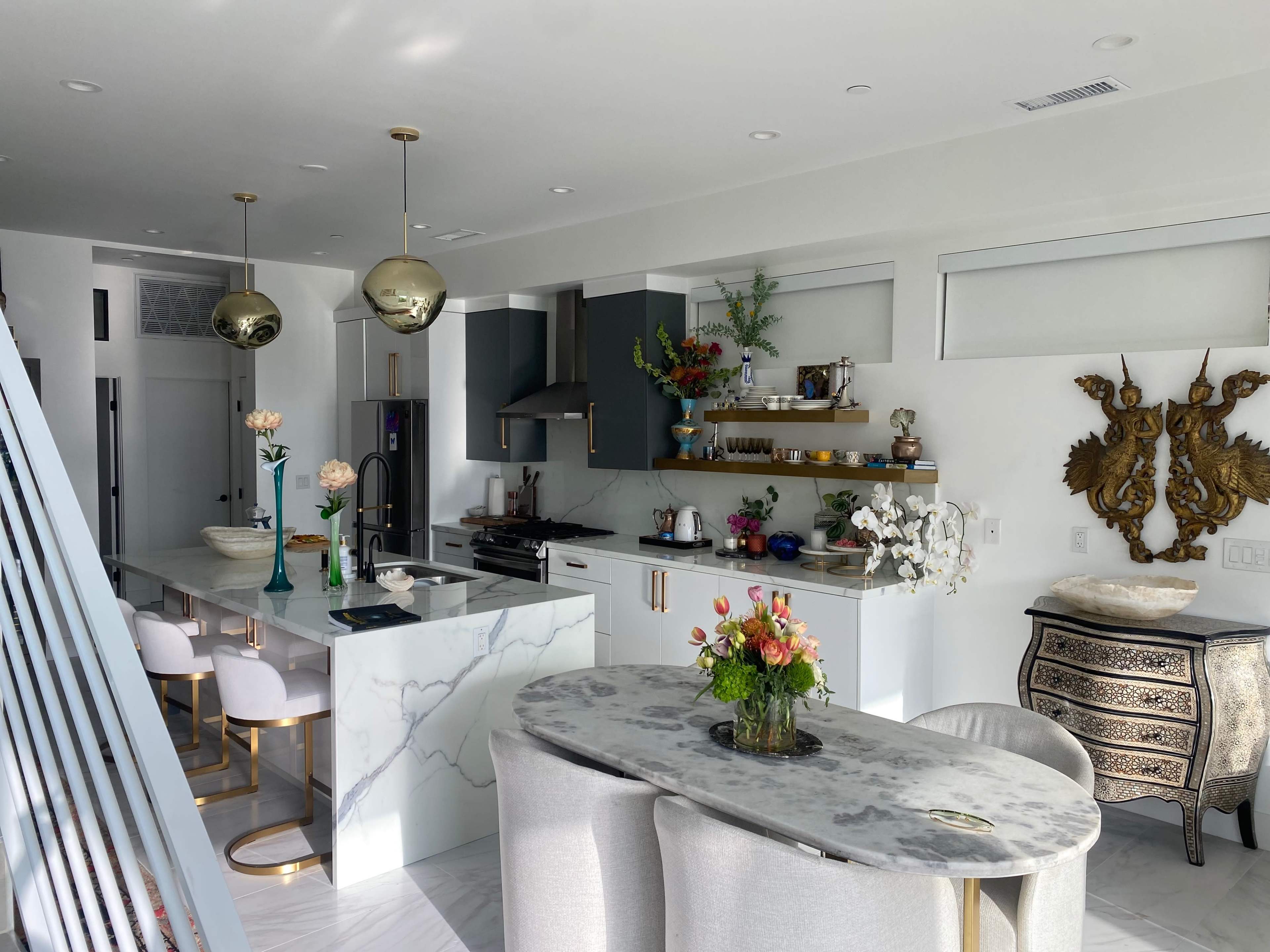 A modern kitchen with marble countertops, gold light fixtures, and a dining area featuring a round table and upholstered chairs.