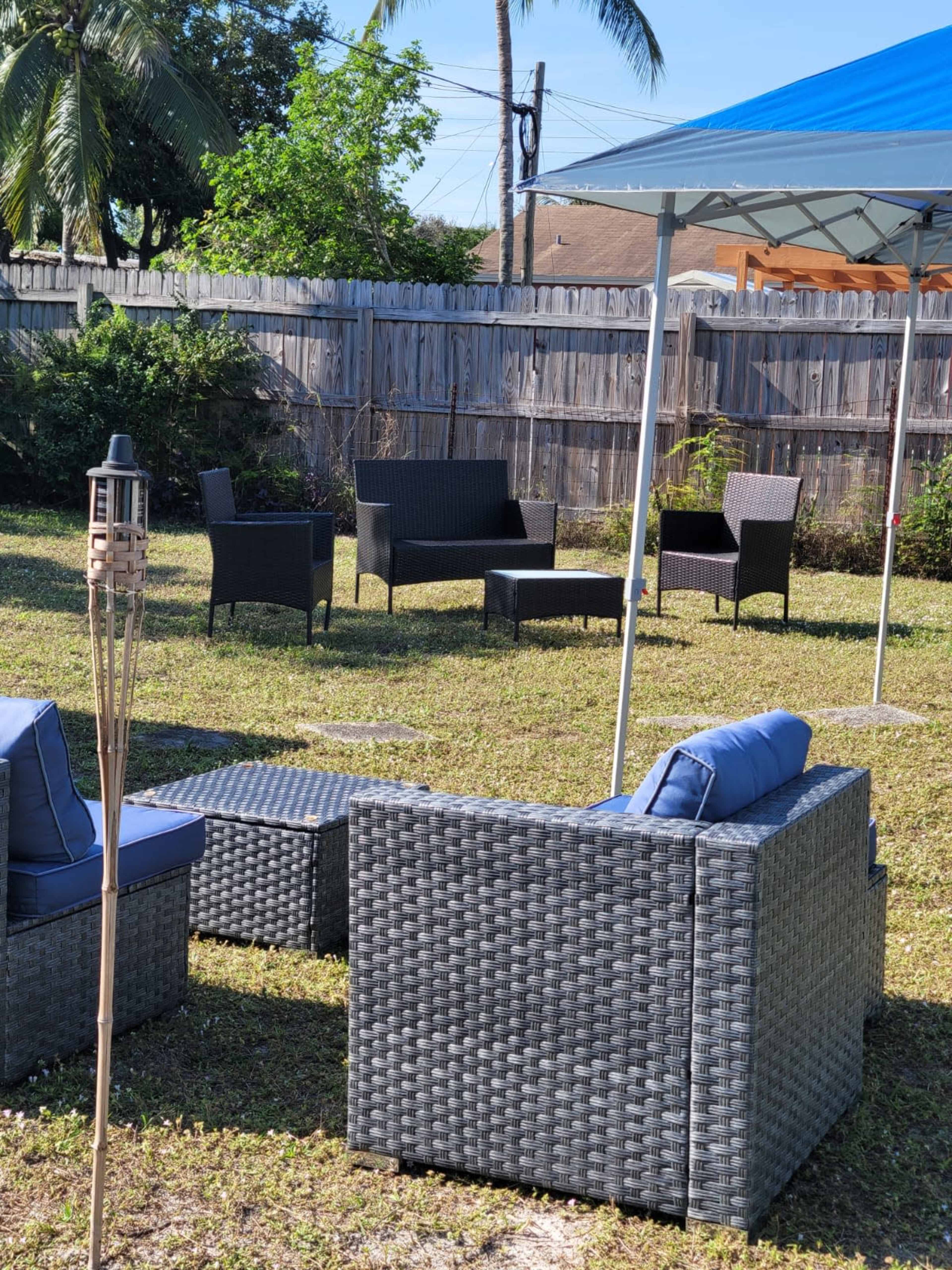 A backyard setup with several outdoor wicker chairs and tables arranged on green grass under a blue canopy.