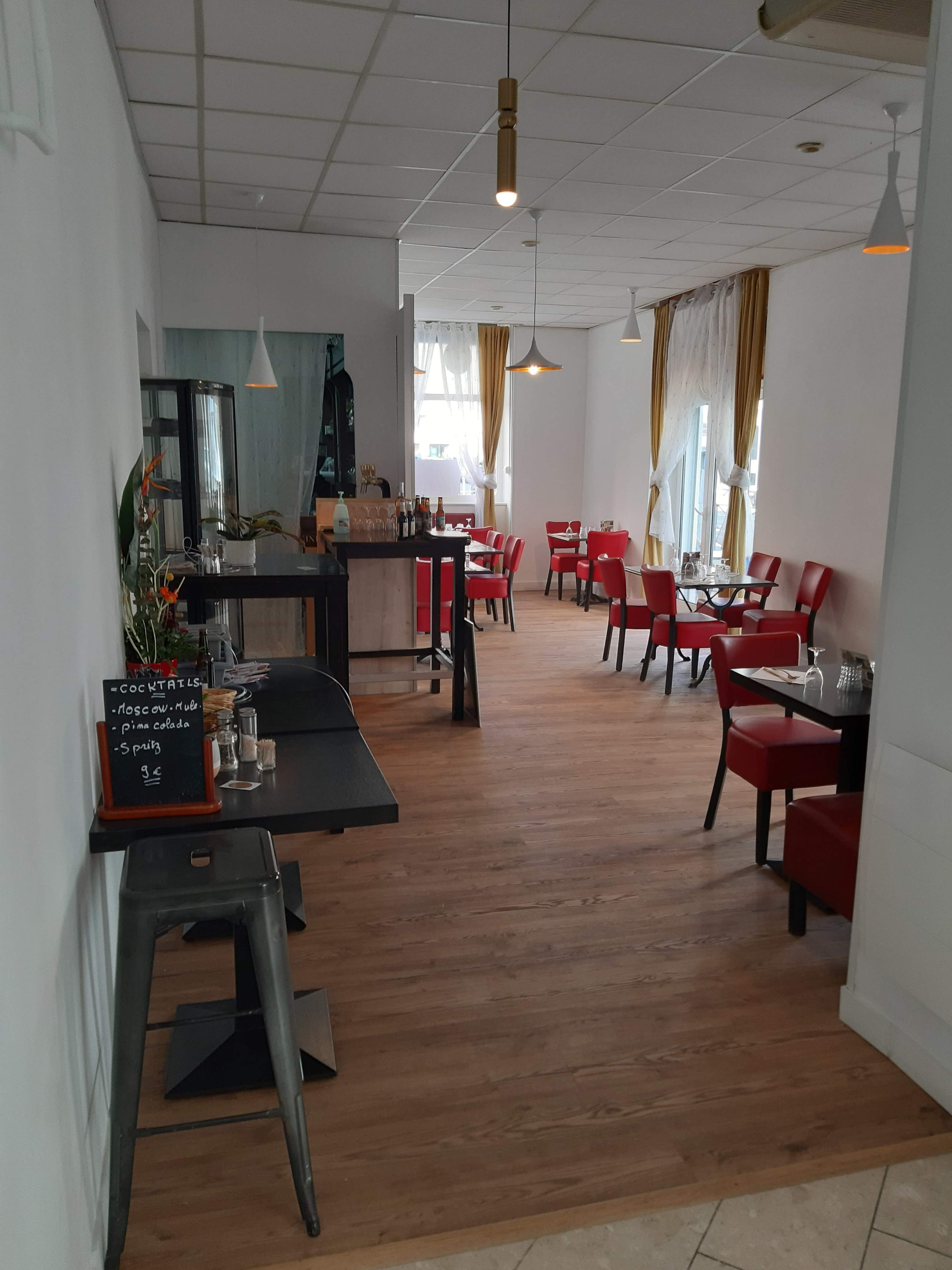 The image shows a spacious restaurant interior featuring red chairs, wooden flooring, and tables arranged along the walls.