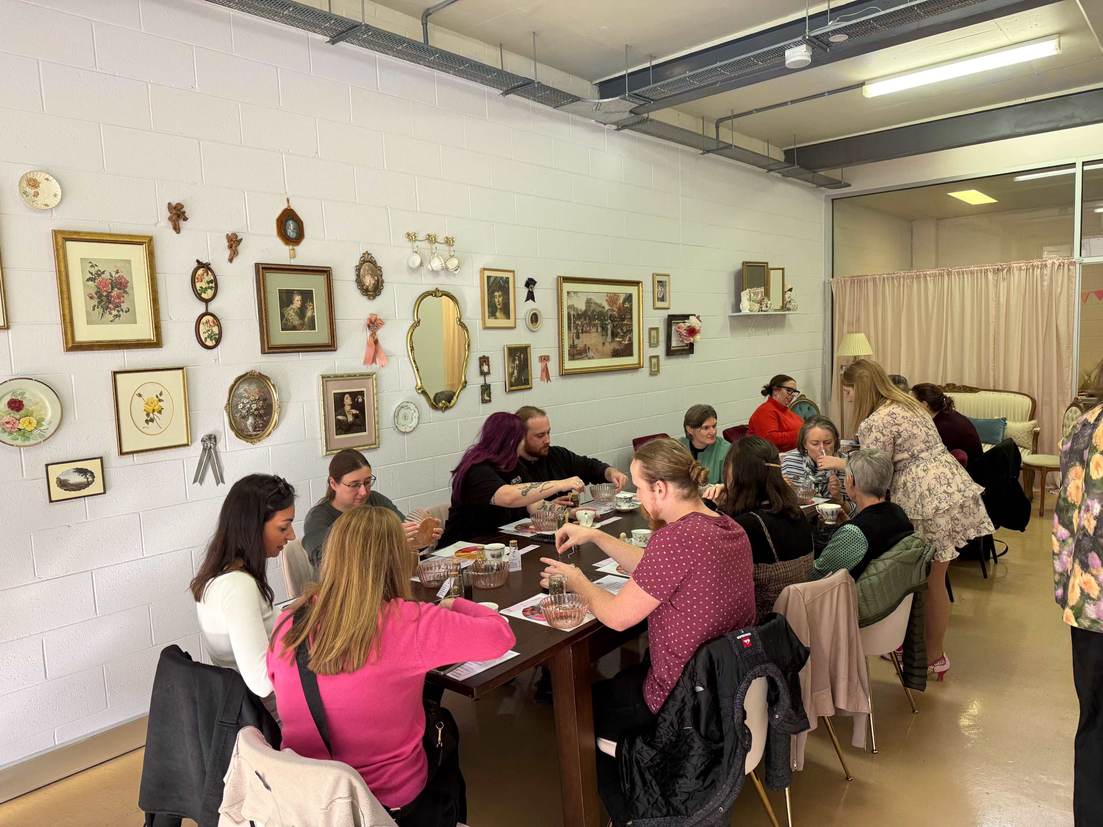 A group of people are seated around a large table in a room decorated with various framed pictures on the wall, engaged in an activity together.