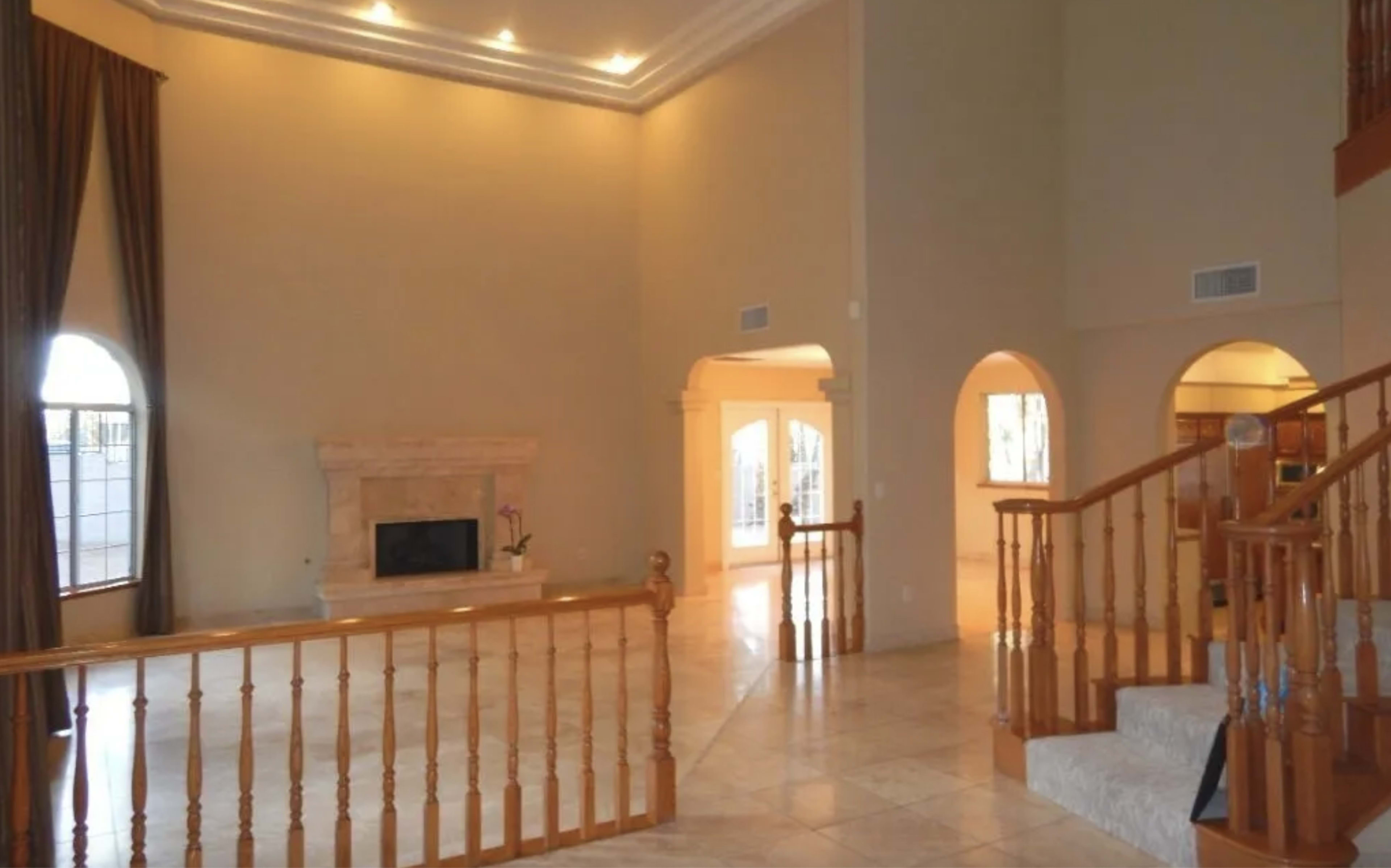 A spacious living room with a fireplace, large windows, and a staircase leading to an upper level.