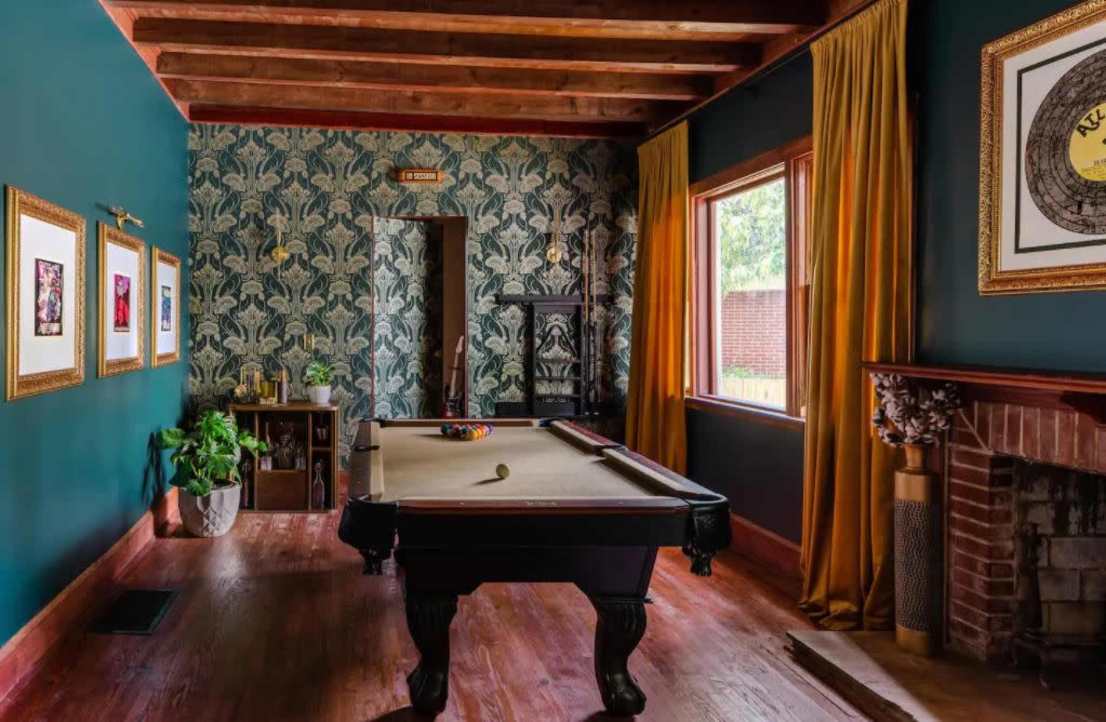 The image shows a game room featuring a pool table, green walls, wooden beams, and framed artwork on the walls.