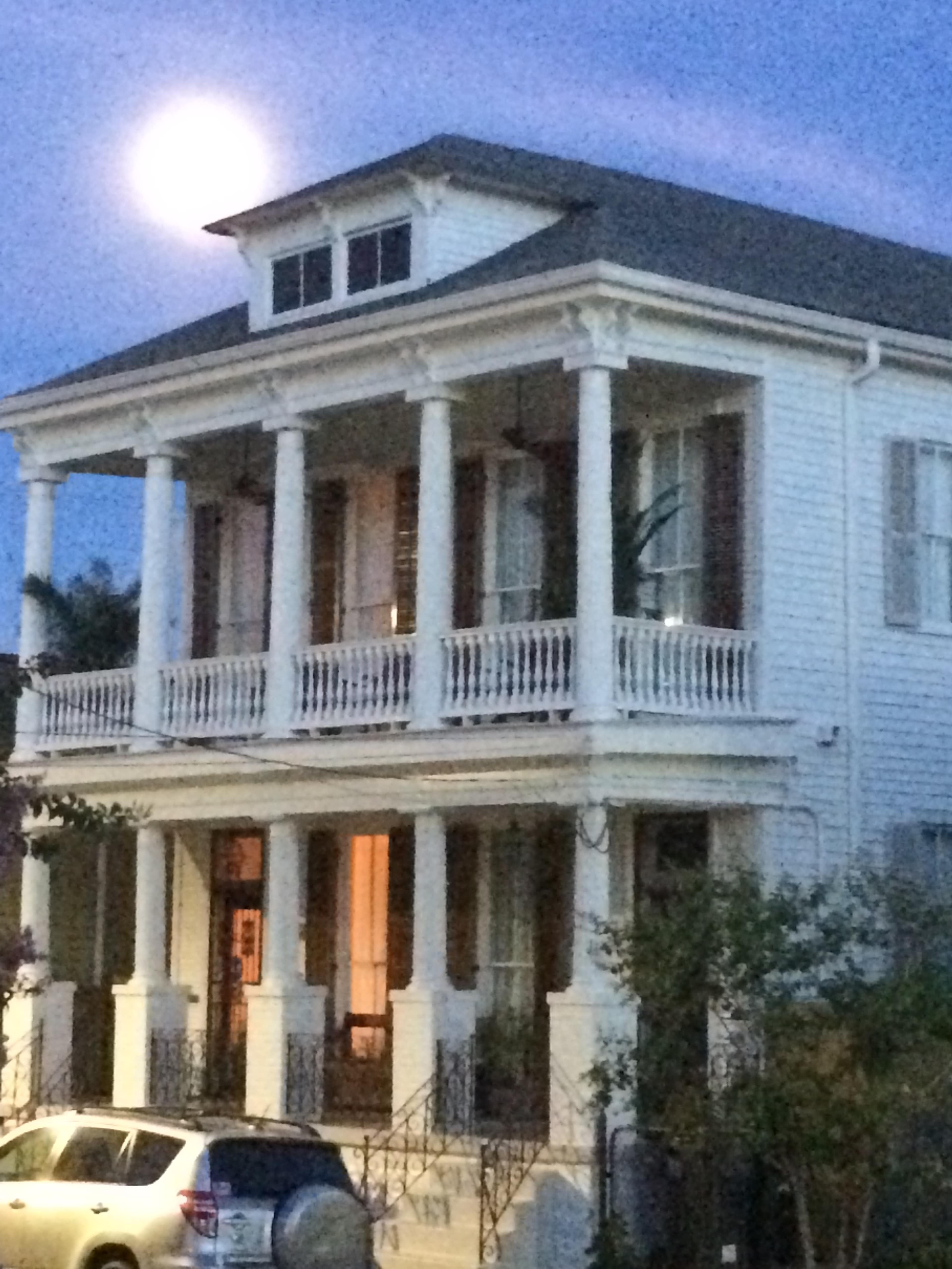 A large two-story white house with prominent columns and a full moon visible in the background.