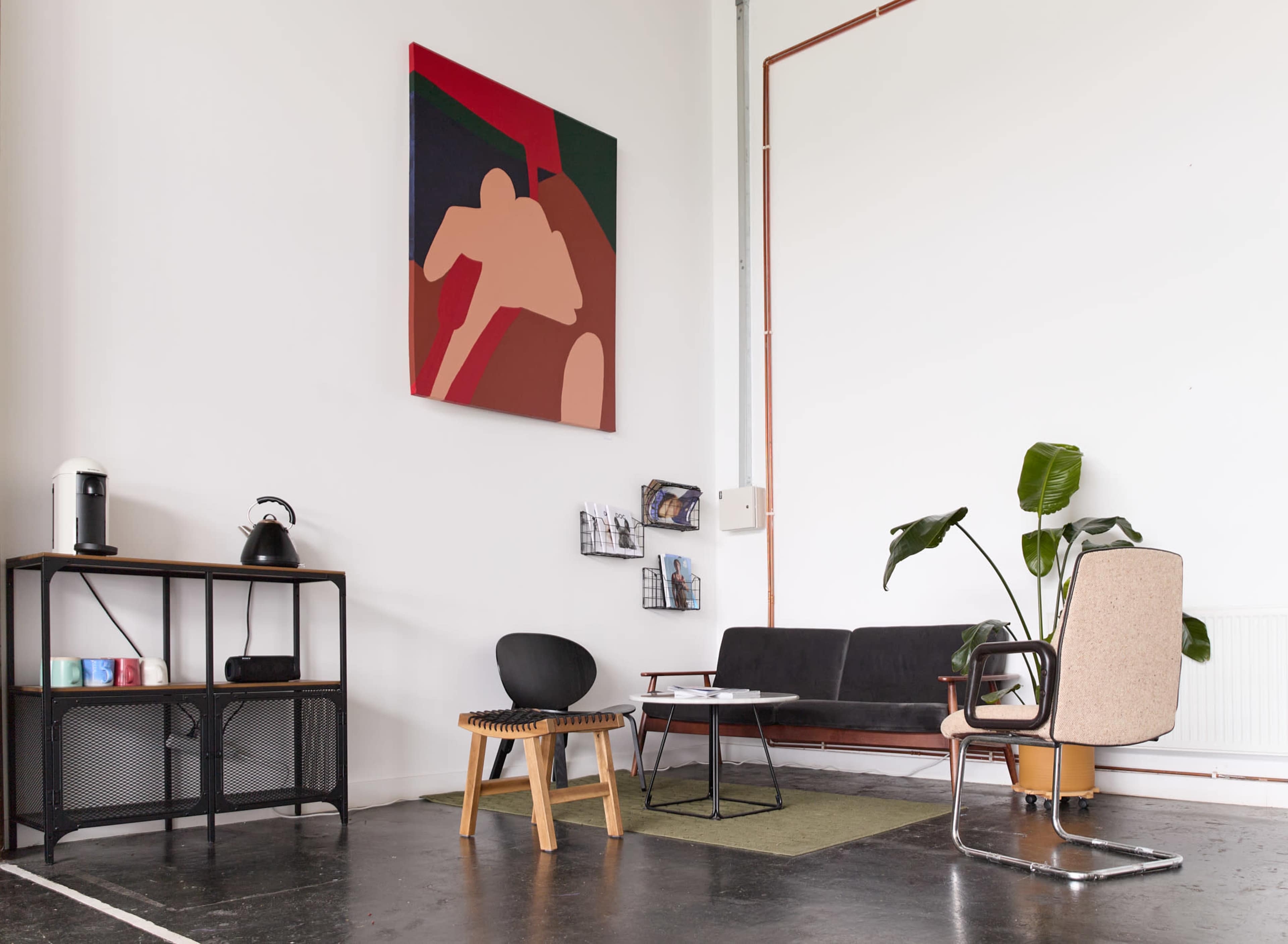 A modern interior space featuring a black sofa, a wooden stool, a contemporary chair, a coffee table, and an abstract wall painting.