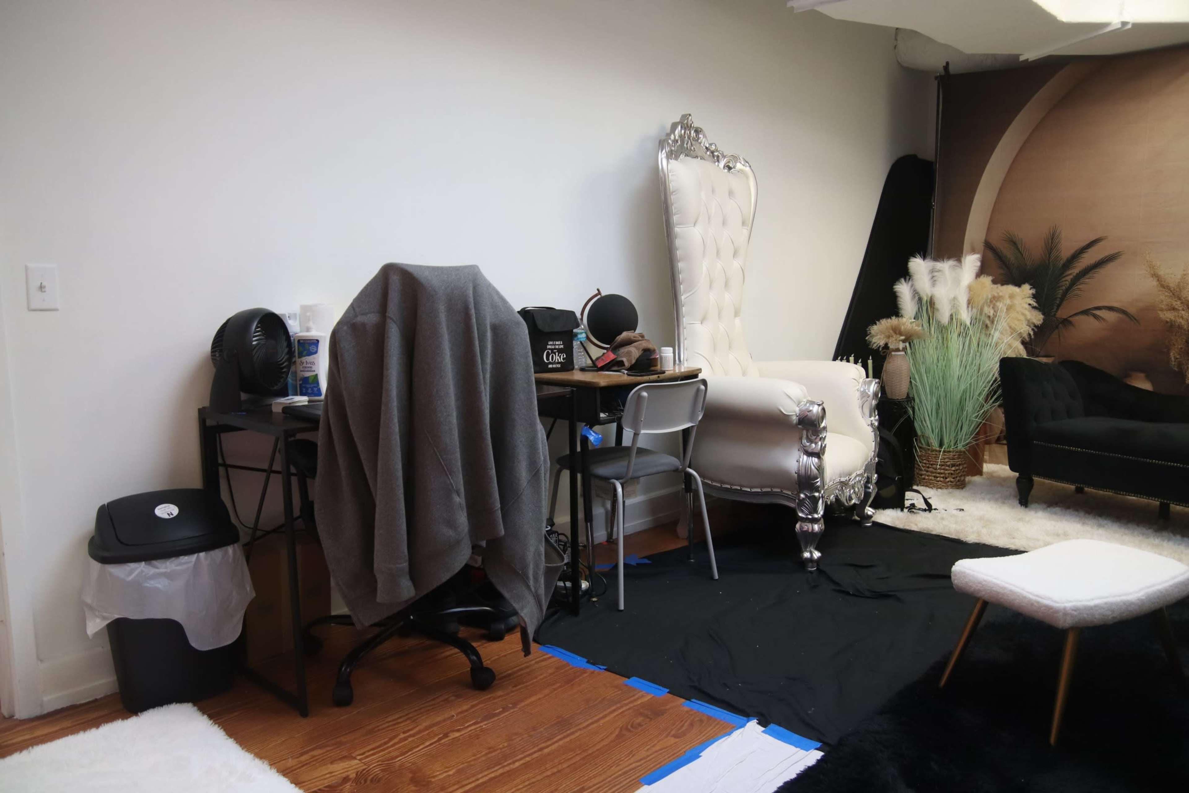 The image shows a room with a desk and chair, a large ornate armchair, and a small table on a black floor covering.