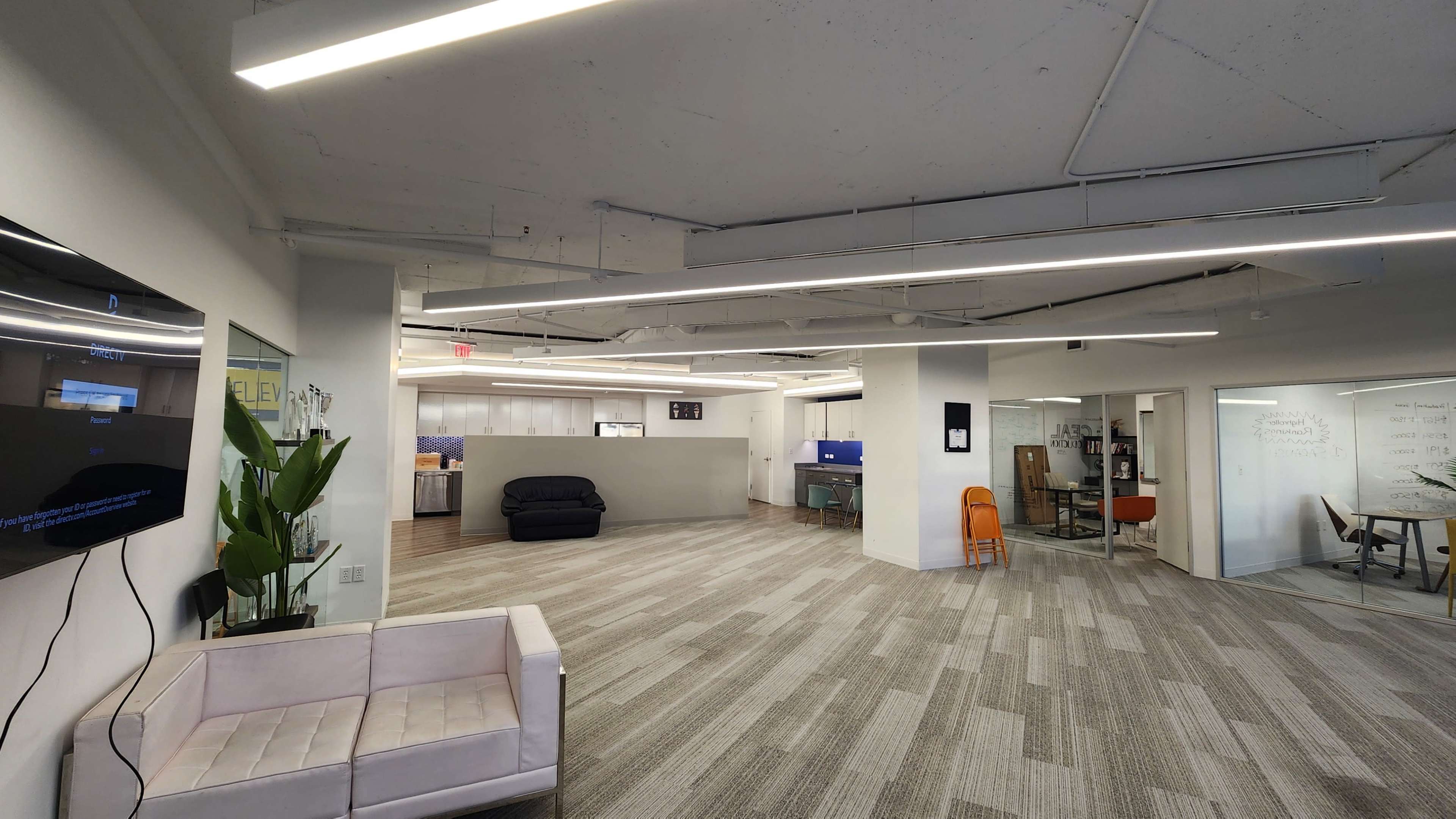 An open office space with modern furniture, including a white couch, and areas for workstations and meetings.