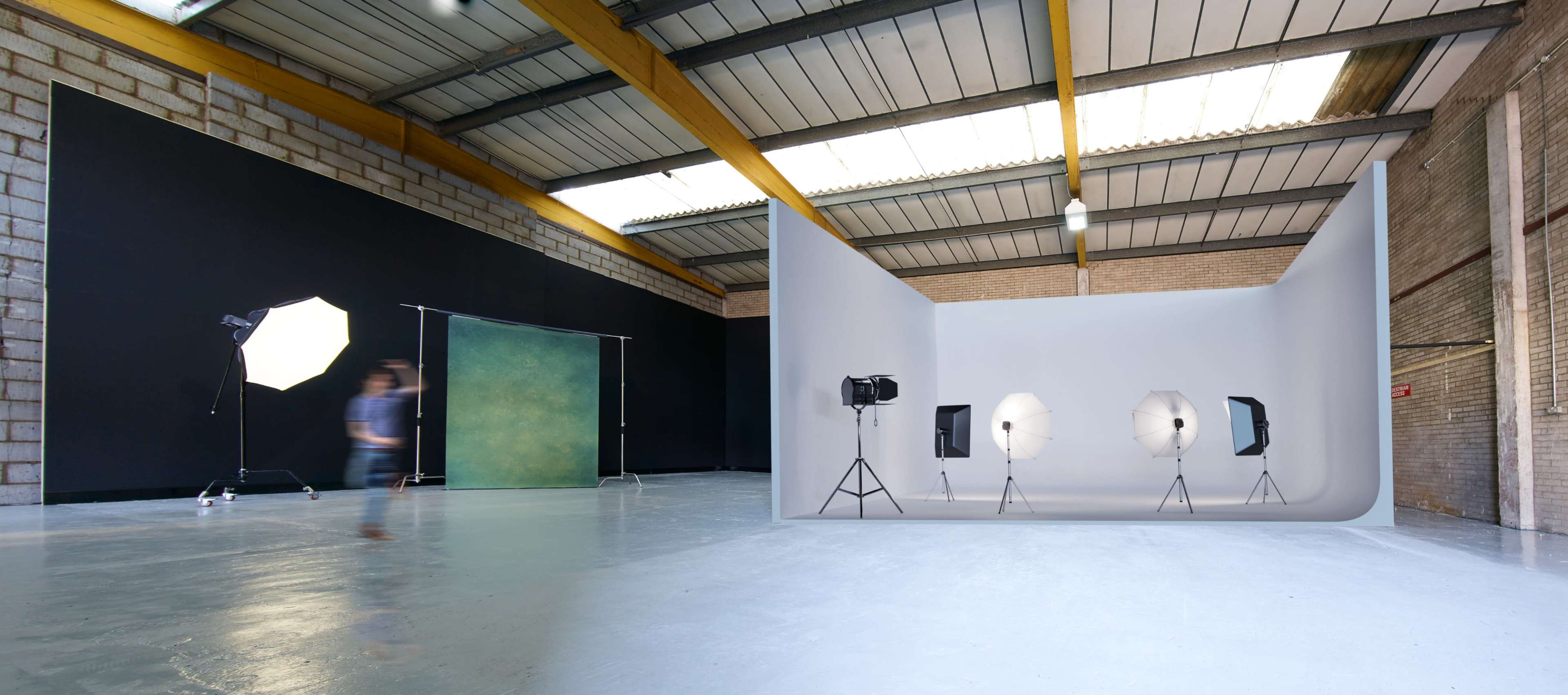 A spacious photography studio with a white backdrop, three studio lights, and a large dark backdrop in the background.