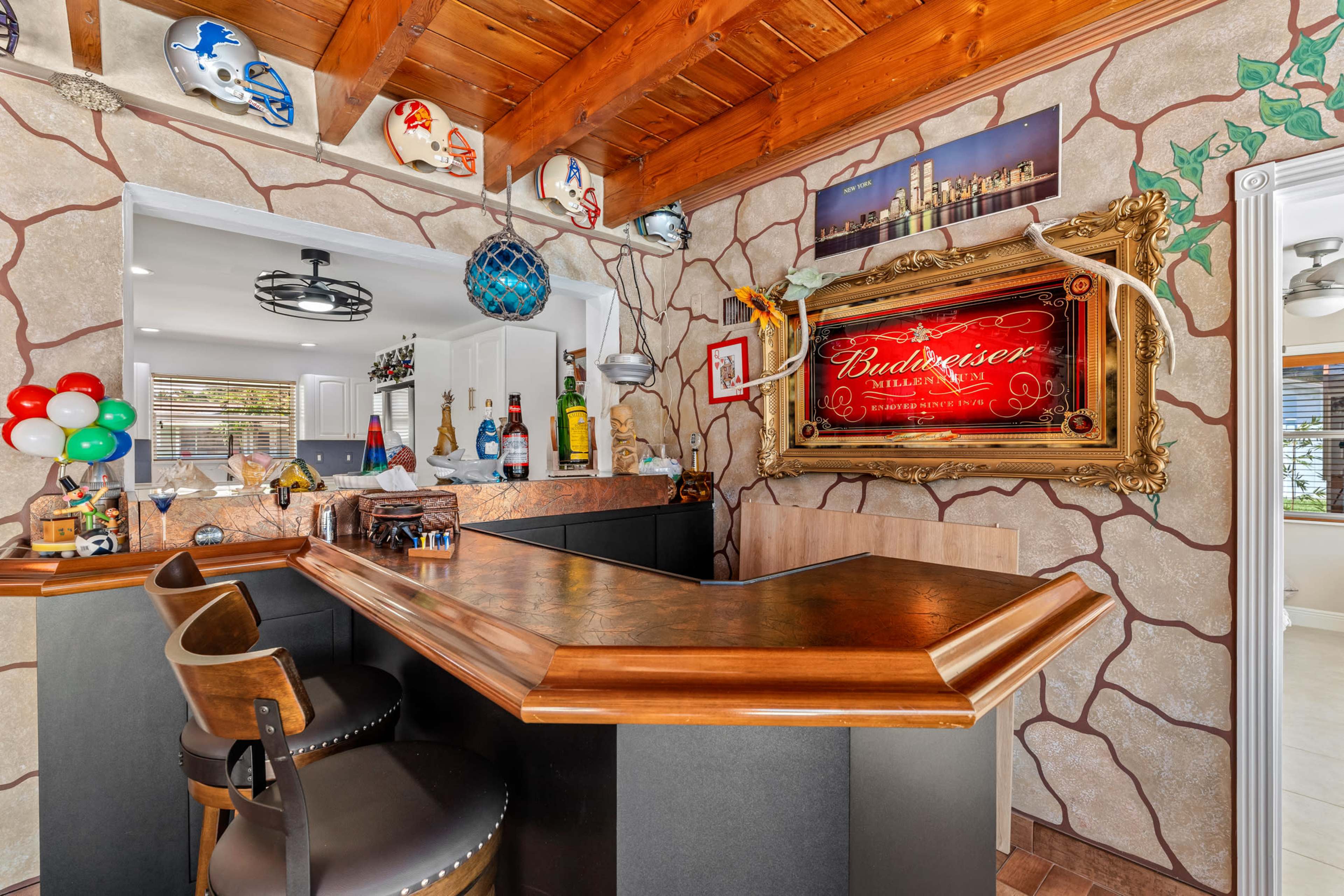 The image shows a home bar area with a hexagonal counter, adorned with decor including a "Budweiser" sign and various collectibles on the walls.