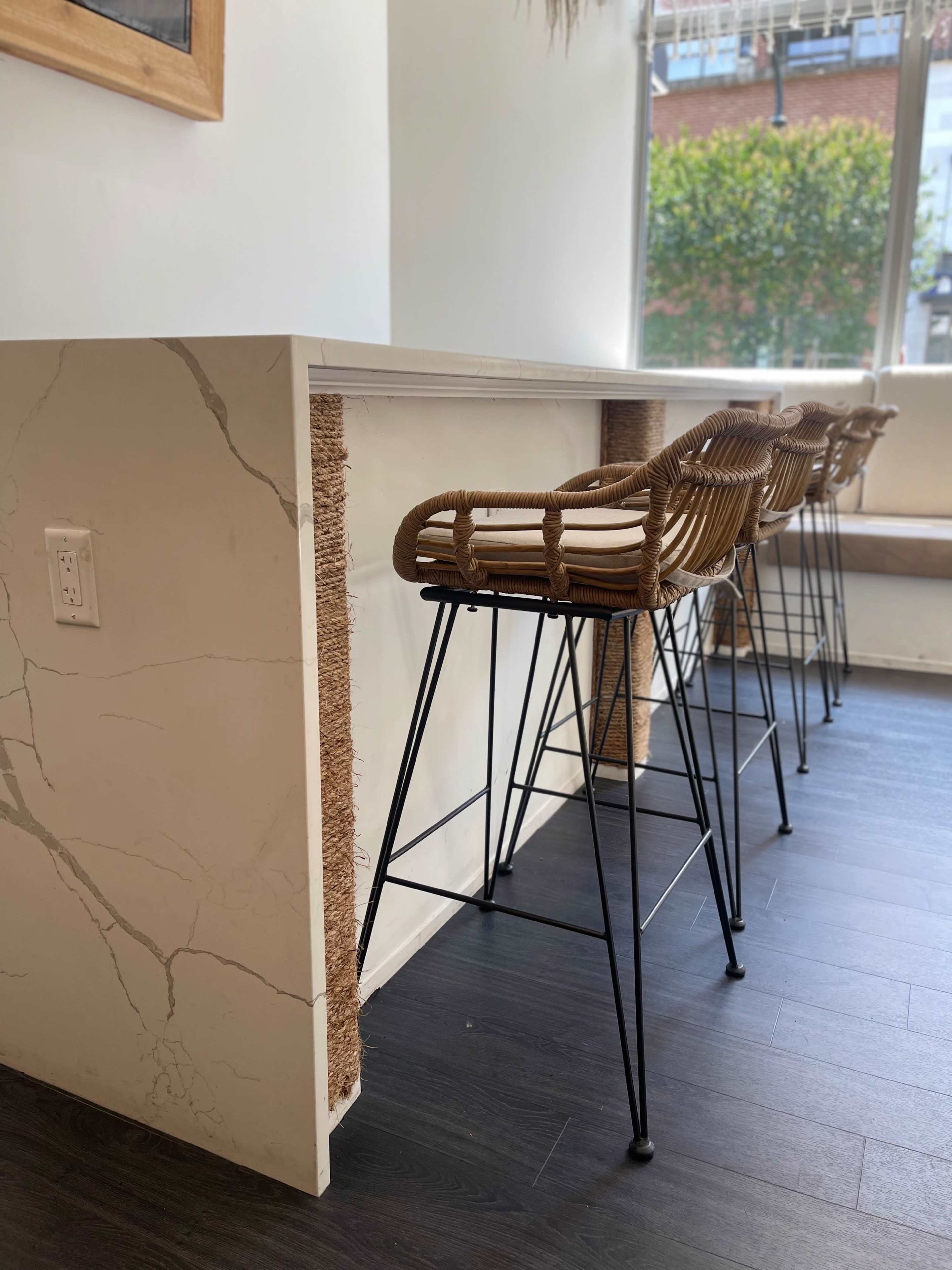 A minimalist bar counter with four woven bar stools placed against it, set in a brightly lit room.