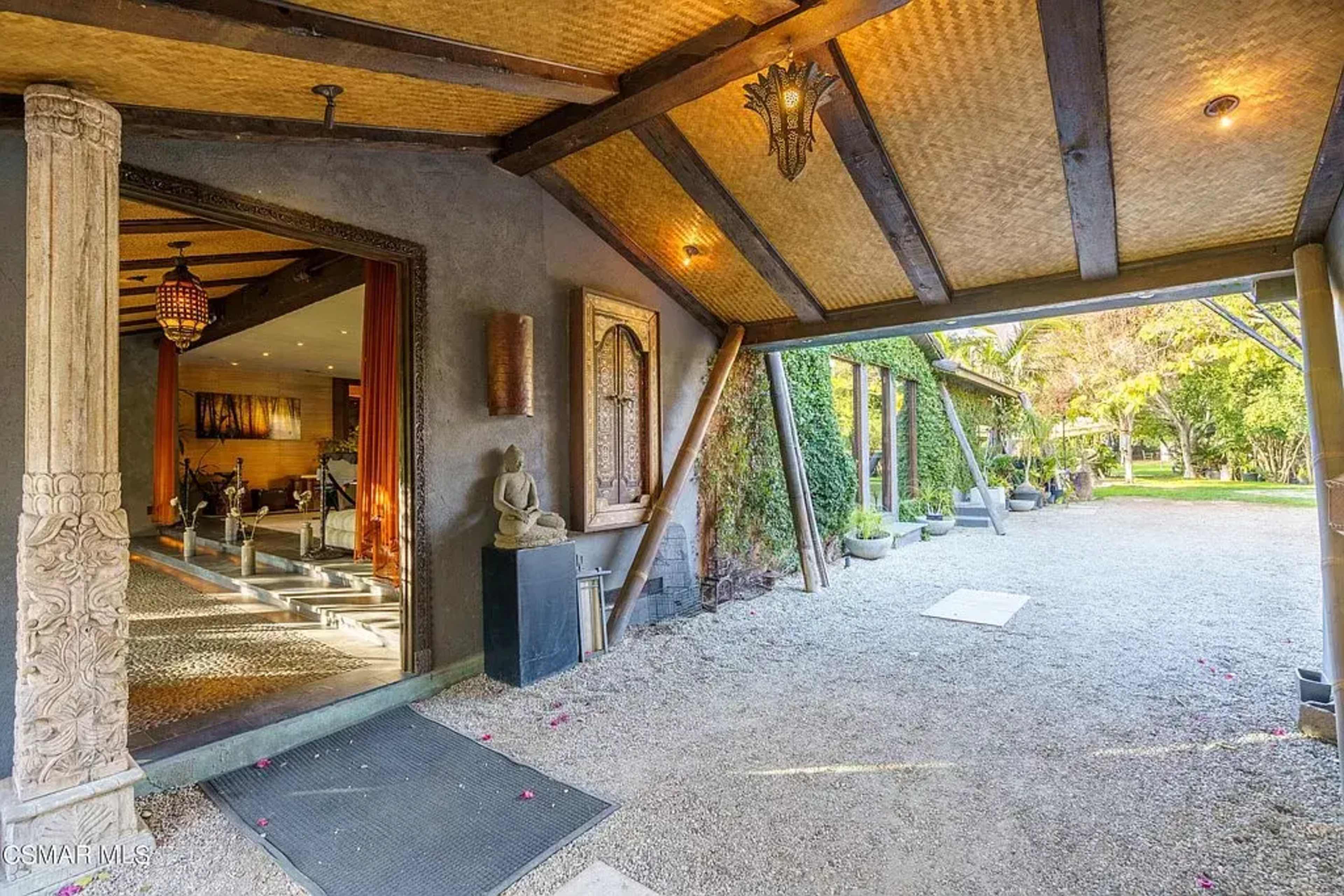 The image shows an entrance area with a covered porch leading into a spacious, landscaped garden.