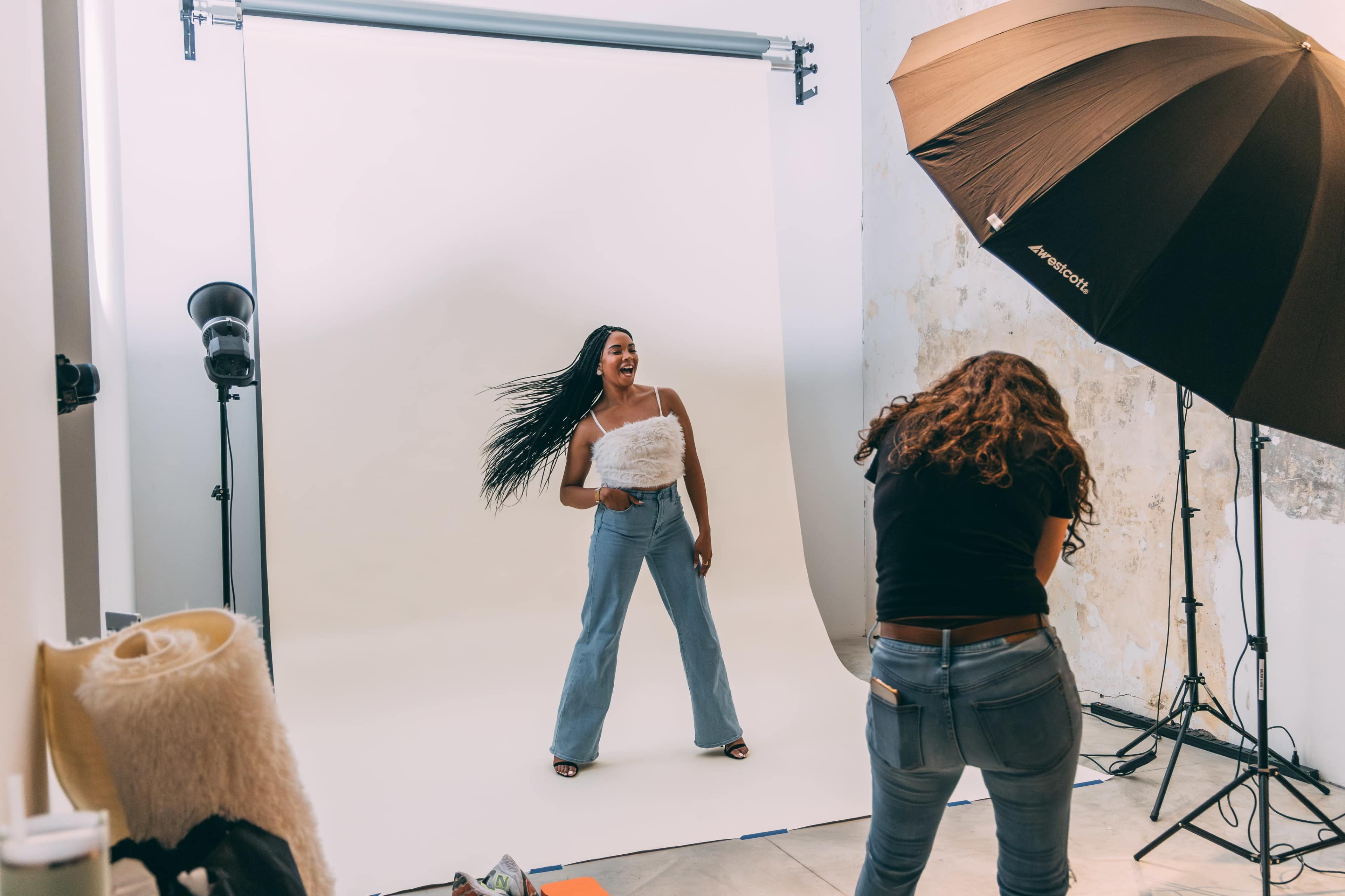 A model poses against a plain backdrop while a photographer captures her image in a studio setting.