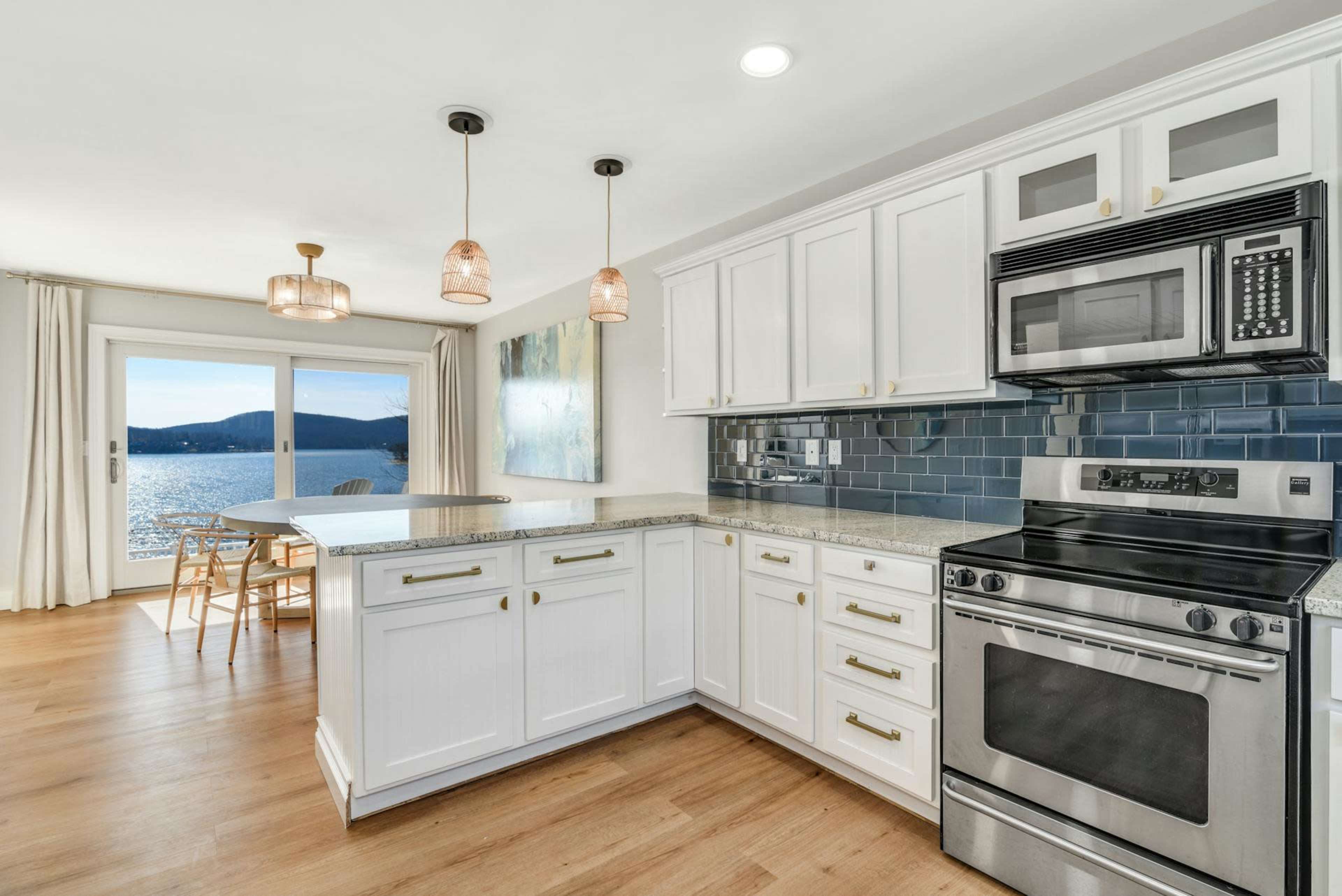 A modern kitchen features white cabinetry, stainless steel appliances, and a view of a lake through large windows.