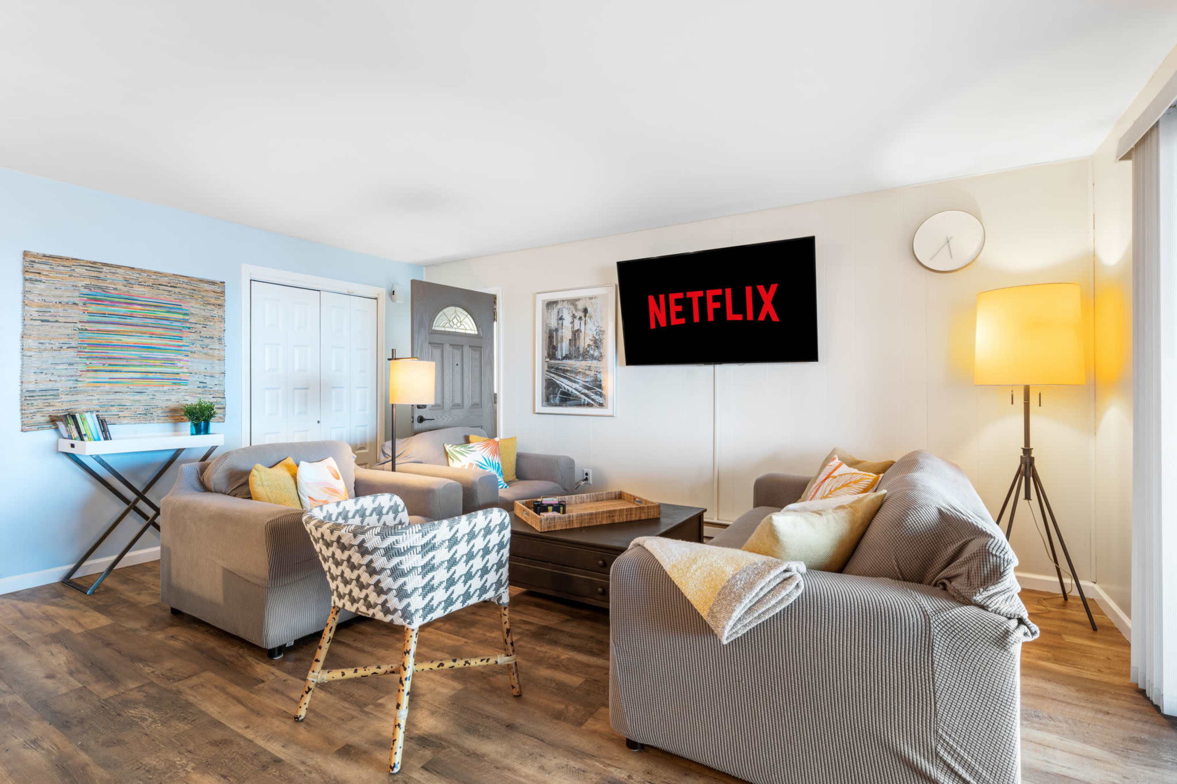 A modern living room features two armchairs and a sofa arranged around a coffee table, with a television displaying the Netflix logo mounted on the wall.