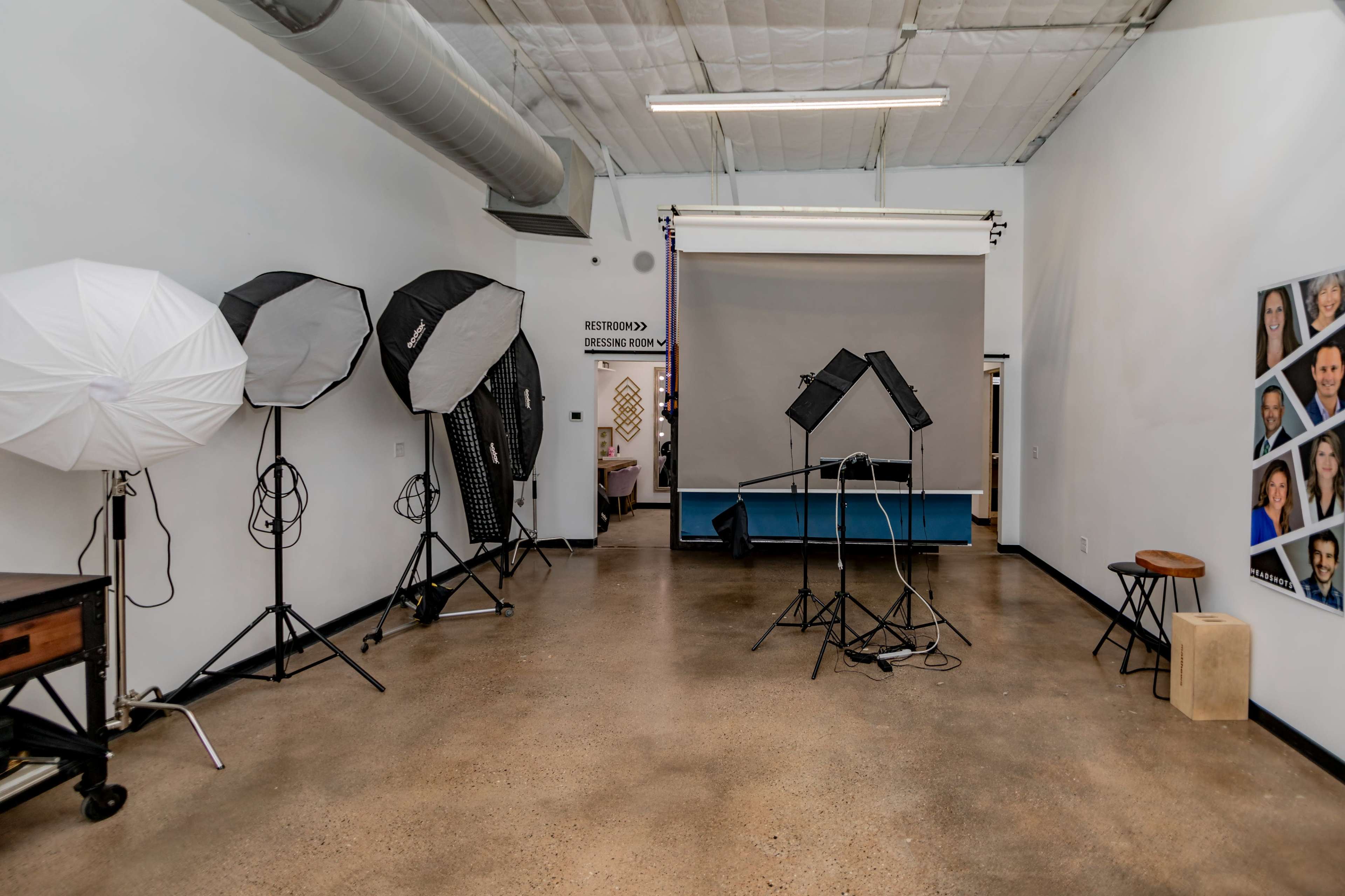 The image shows a spacious photography studio with several lighting equipment setups and a backdrop on display.