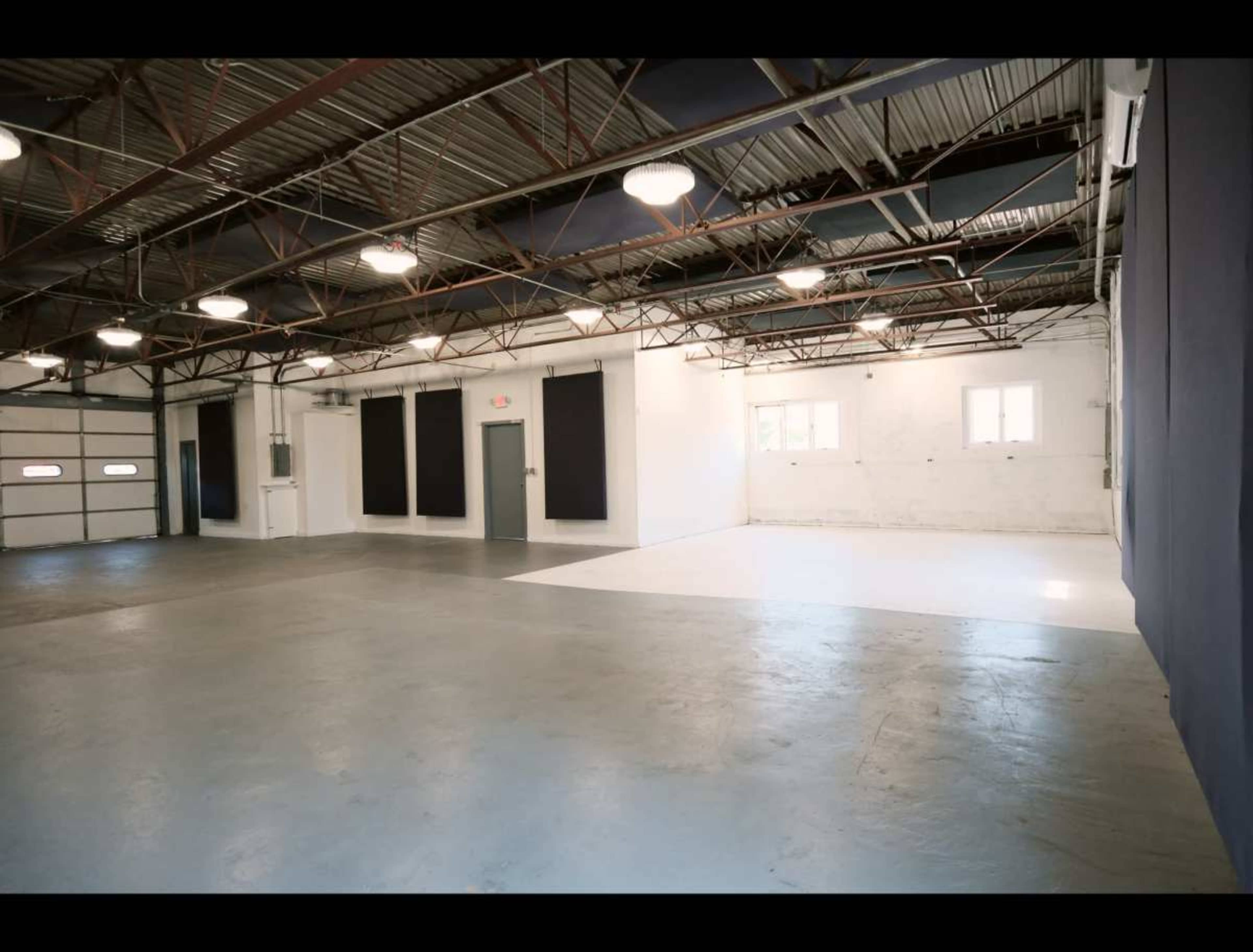 The image shows an industrial space with a concrete floor, high ceilings, and large windows, featuring a mix of white and black walls.