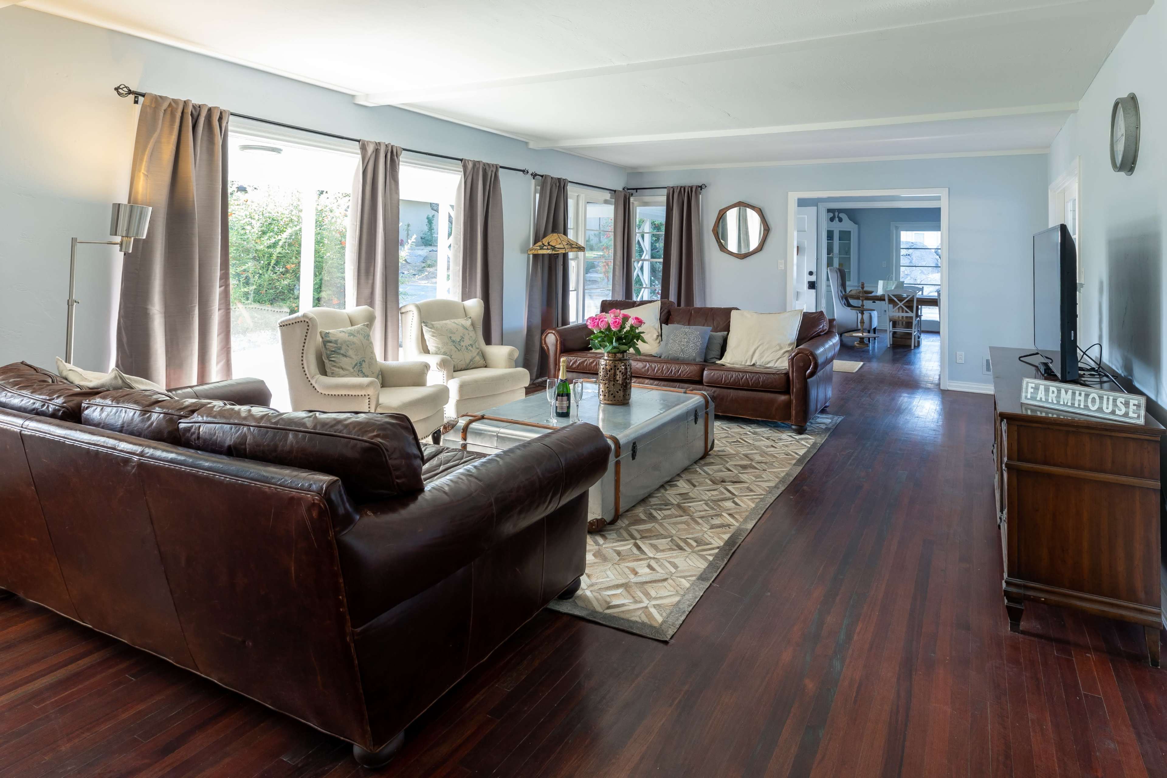 The living room features two leather sofas and a light-colored armchair arranged around a coffee table, with large windows allowing natural light to fill the space.