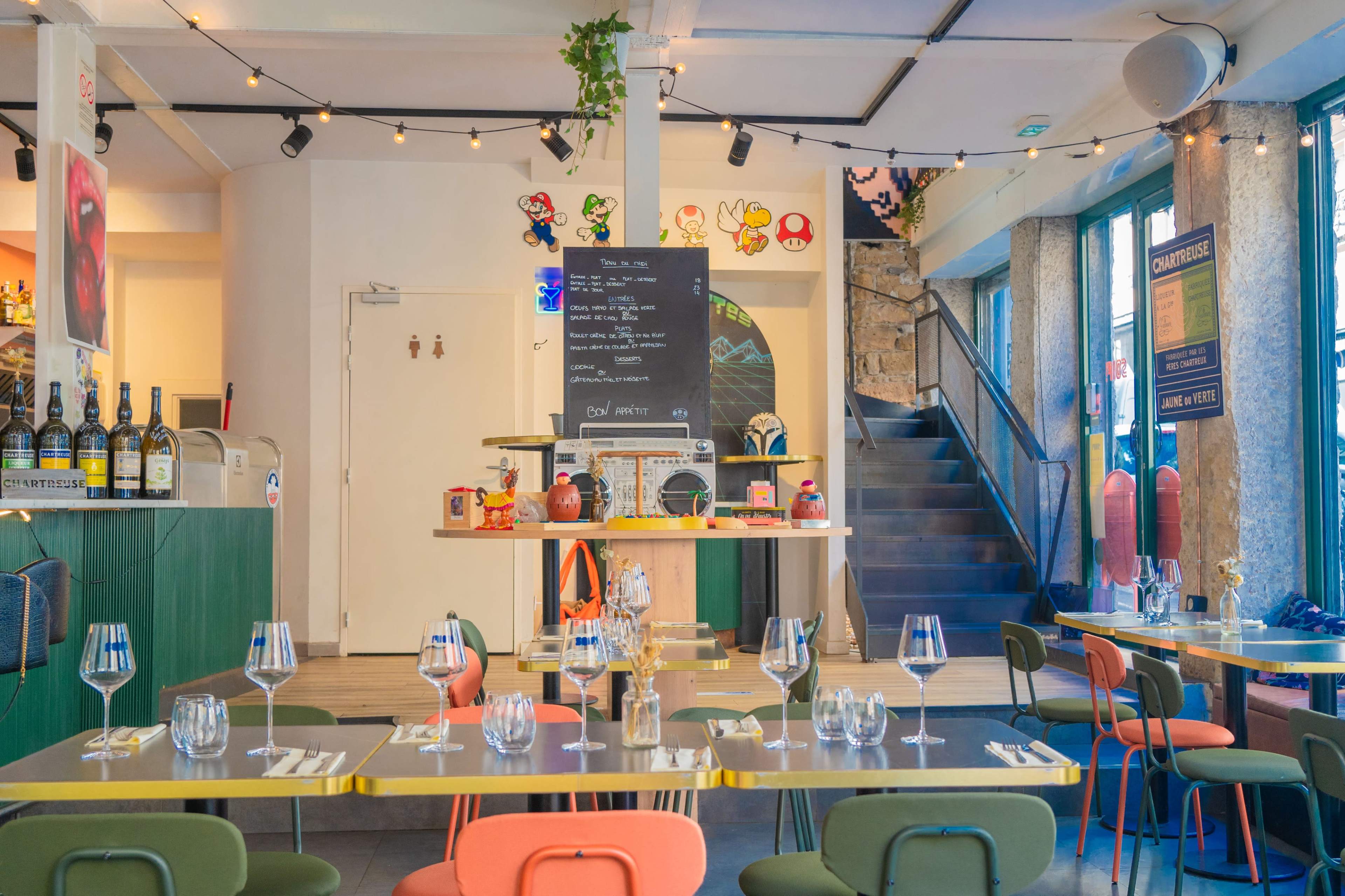 The image shows a brightly lit restaurant interior with colorful chairs, a prominent bar area, and a staircase in the background.