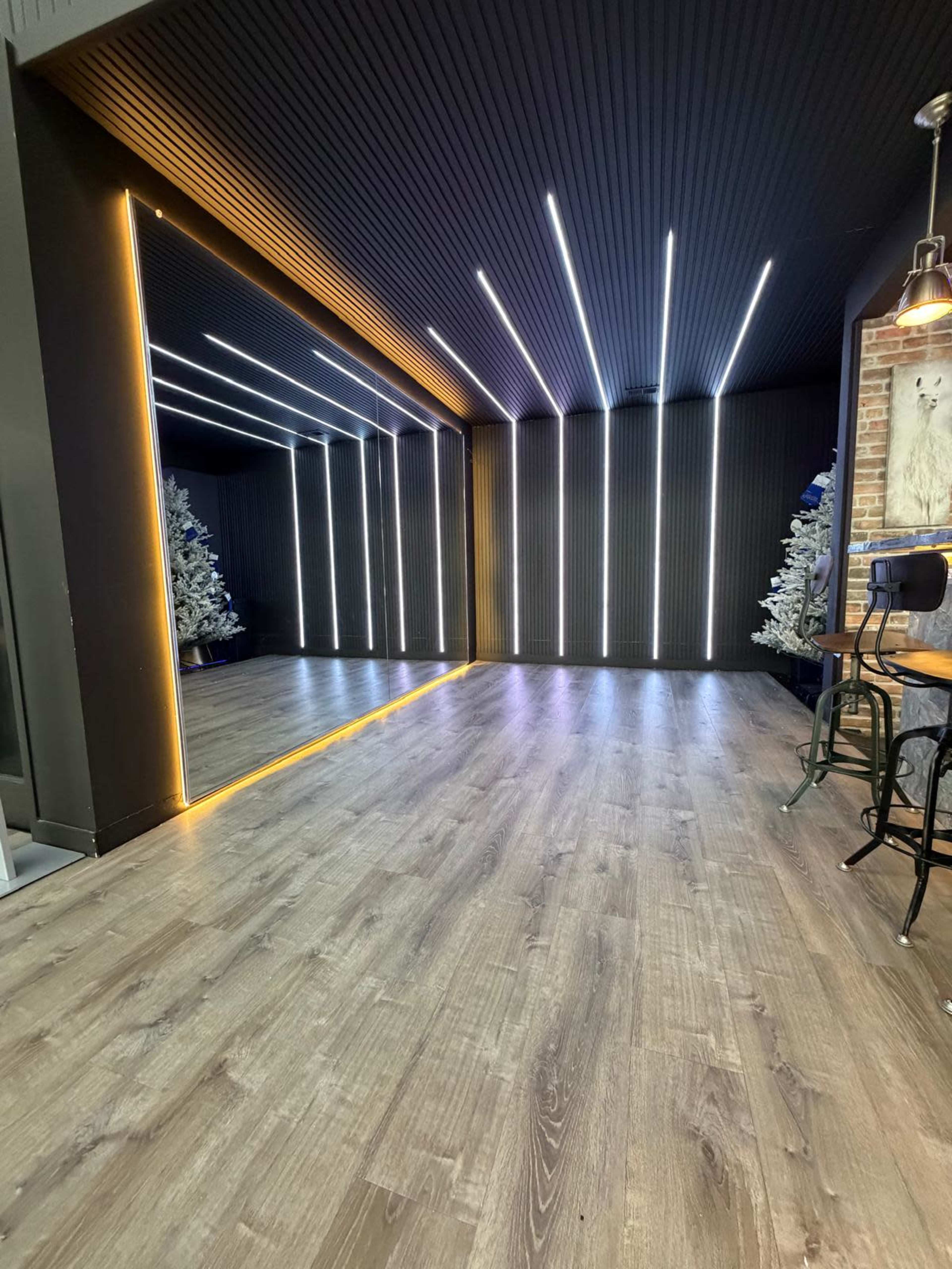 The image shows a modern interior space with linear lighting, a mirrored wall, and decorative Christmas trees in the background.