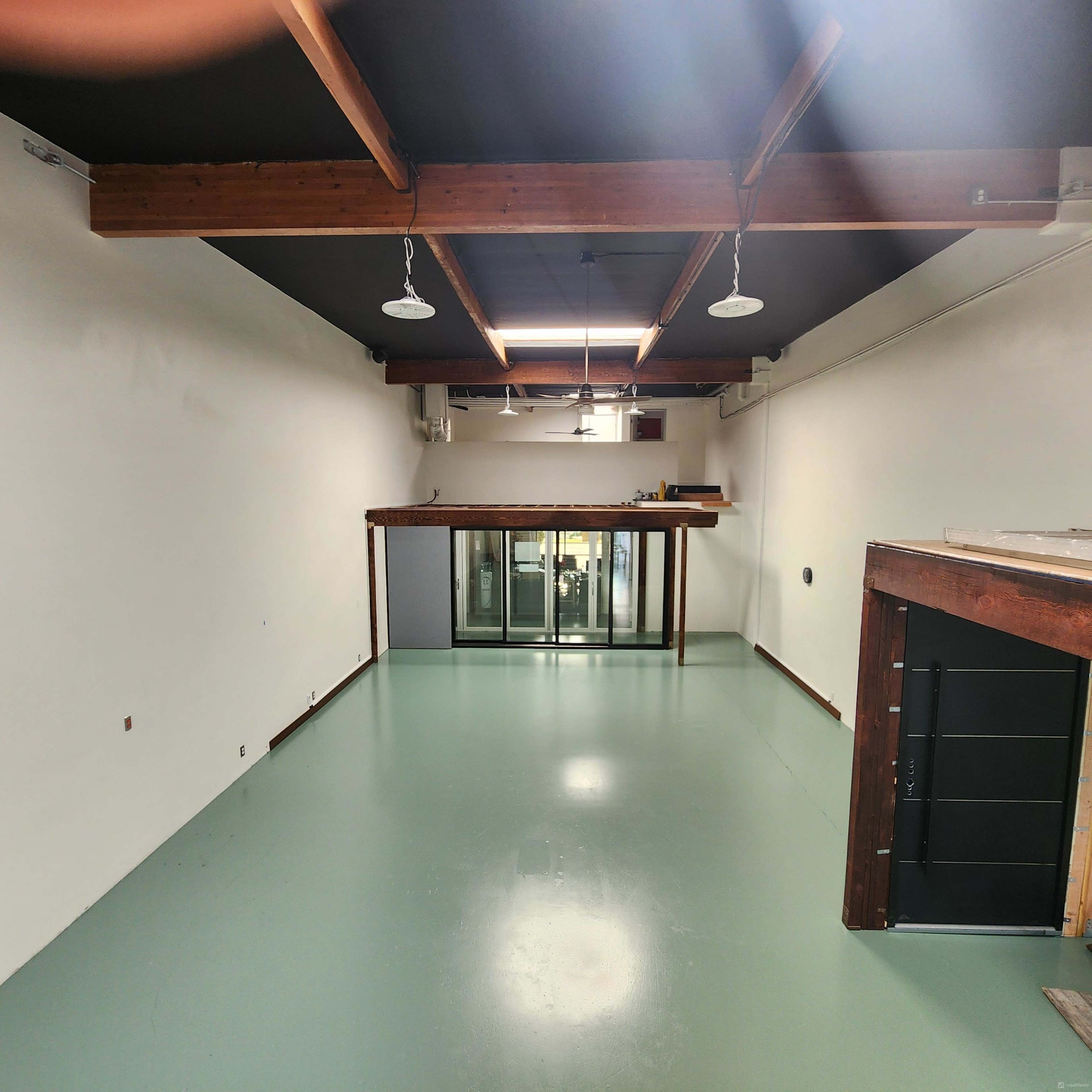 The image shows a spacious, empty interior room with a polished green floor and wooden beams overhead.