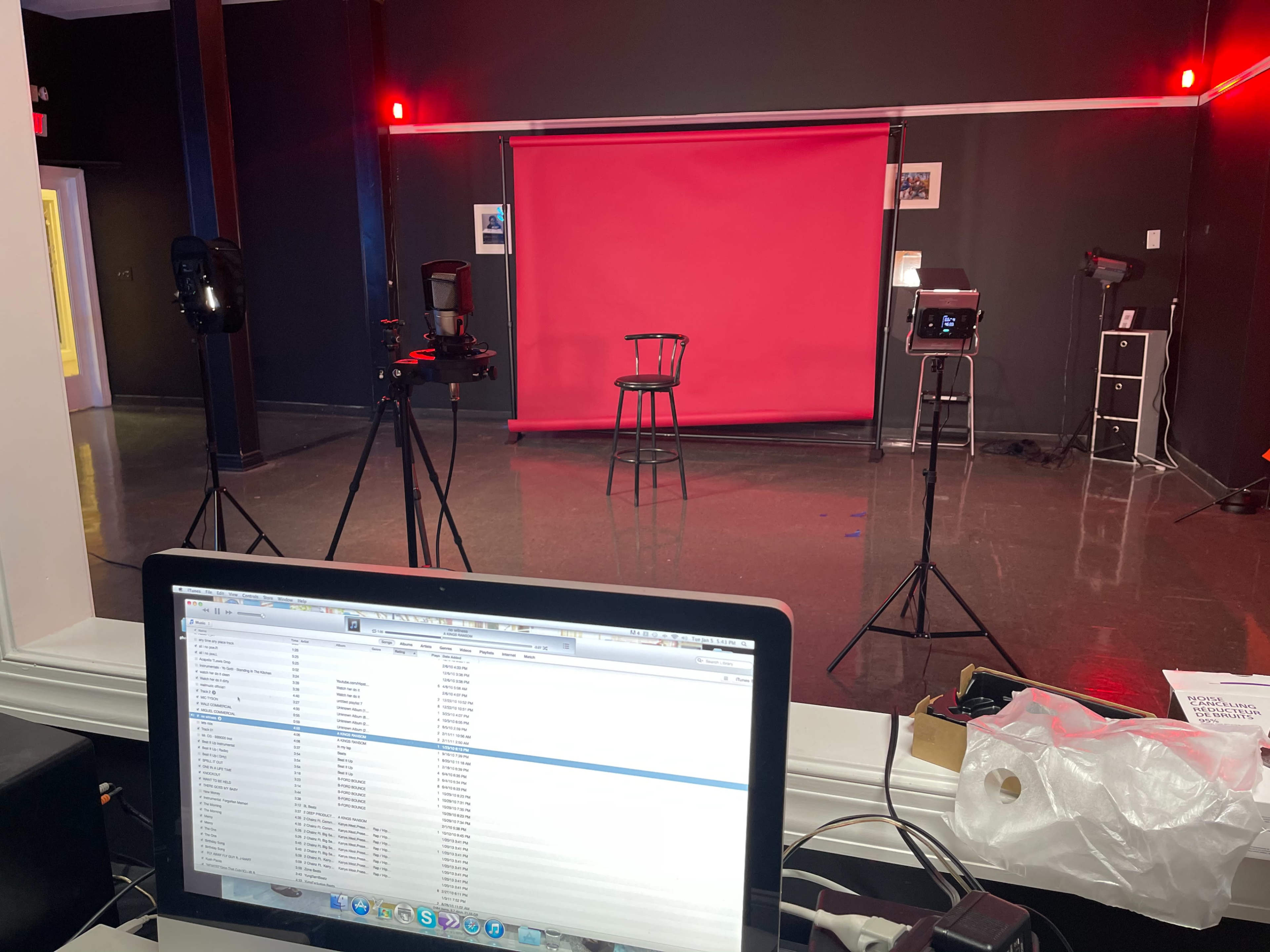 A room with a red backdrop, a black stool, and lighting equipment set up for a recording or performance.