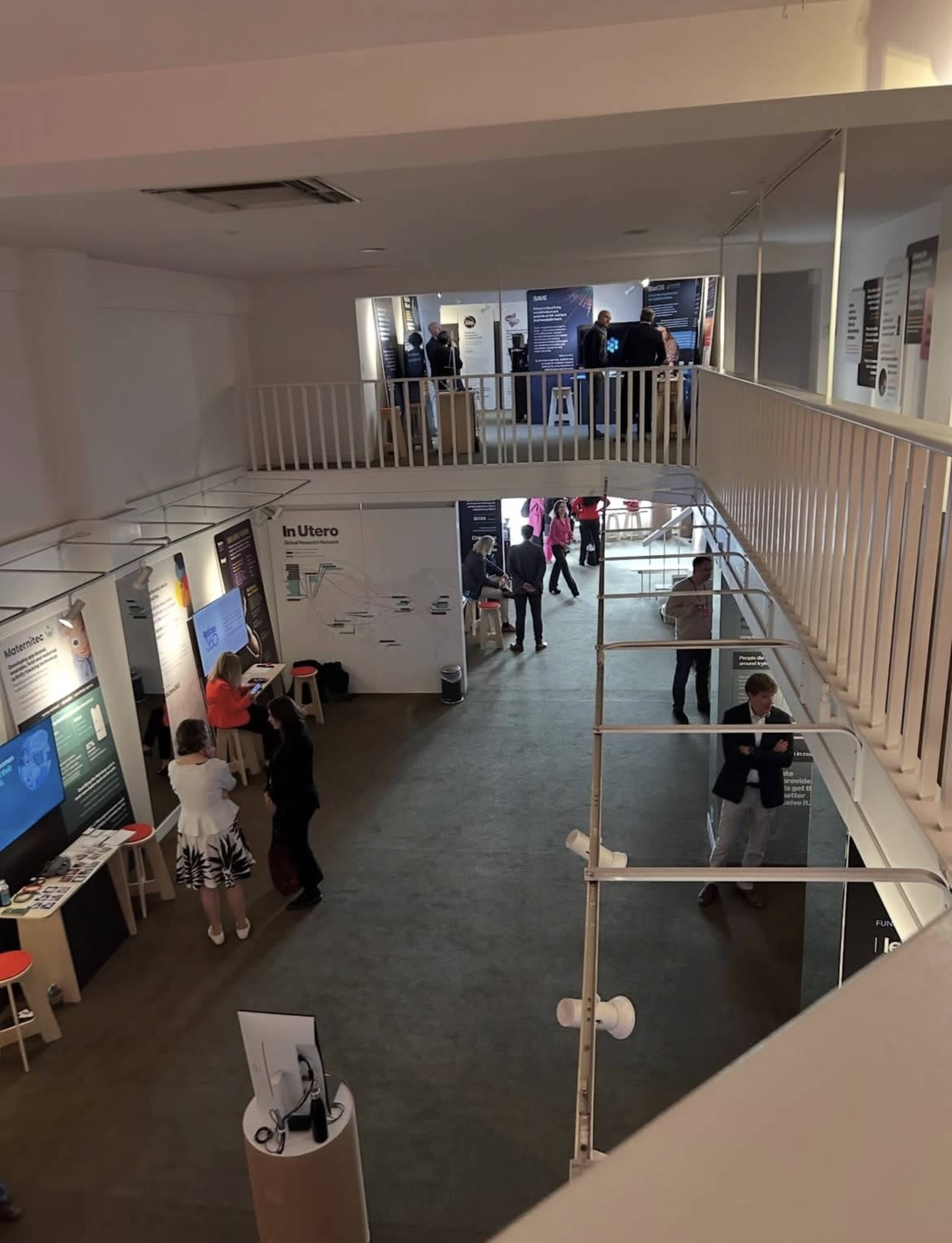 The image shows a multi-level indoor exhibition space with people engaging with displays and presentations.