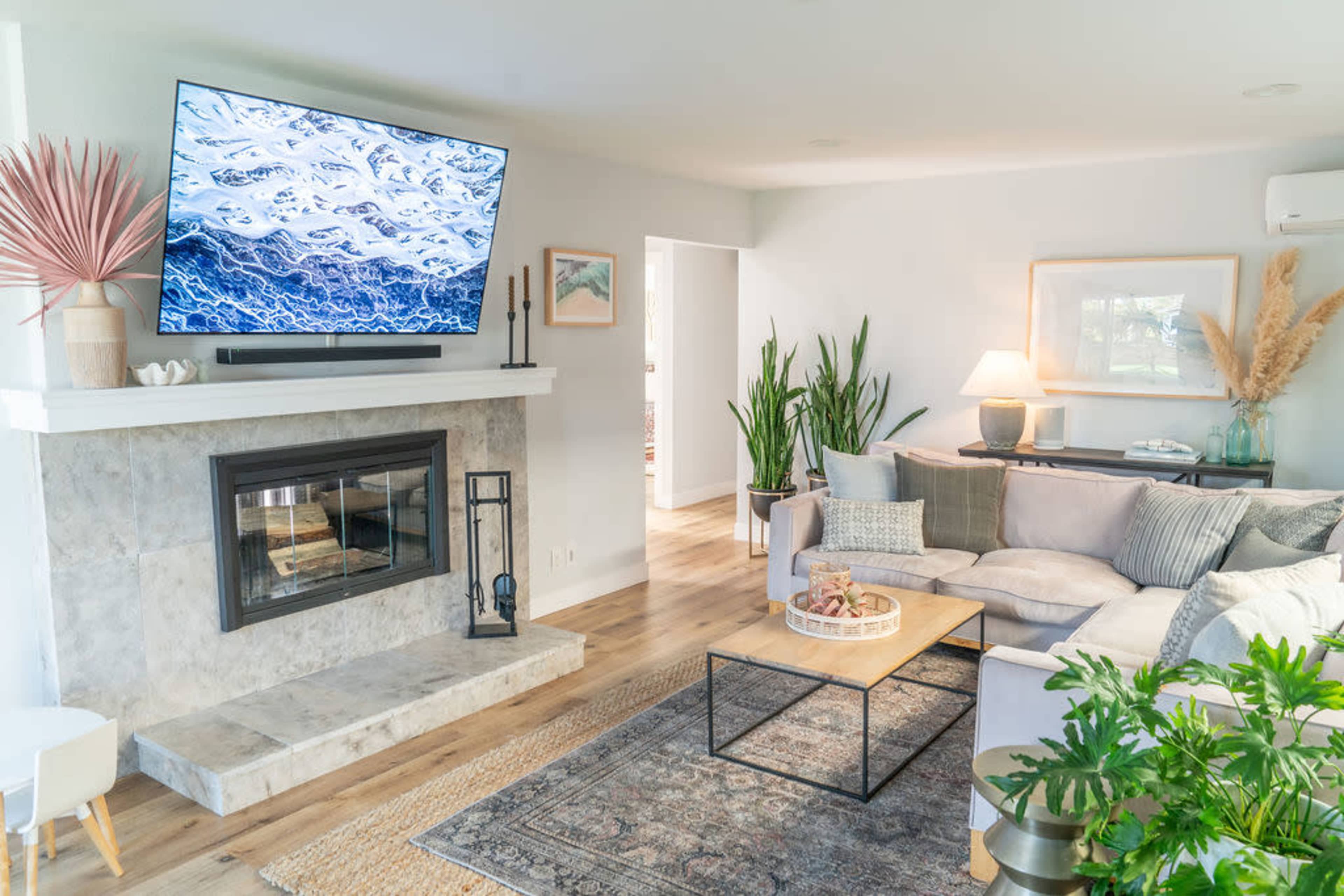 The living room features a large TV mounted above a marble fireplace, with a cozy sectional sofa and a coffee table in front of it.