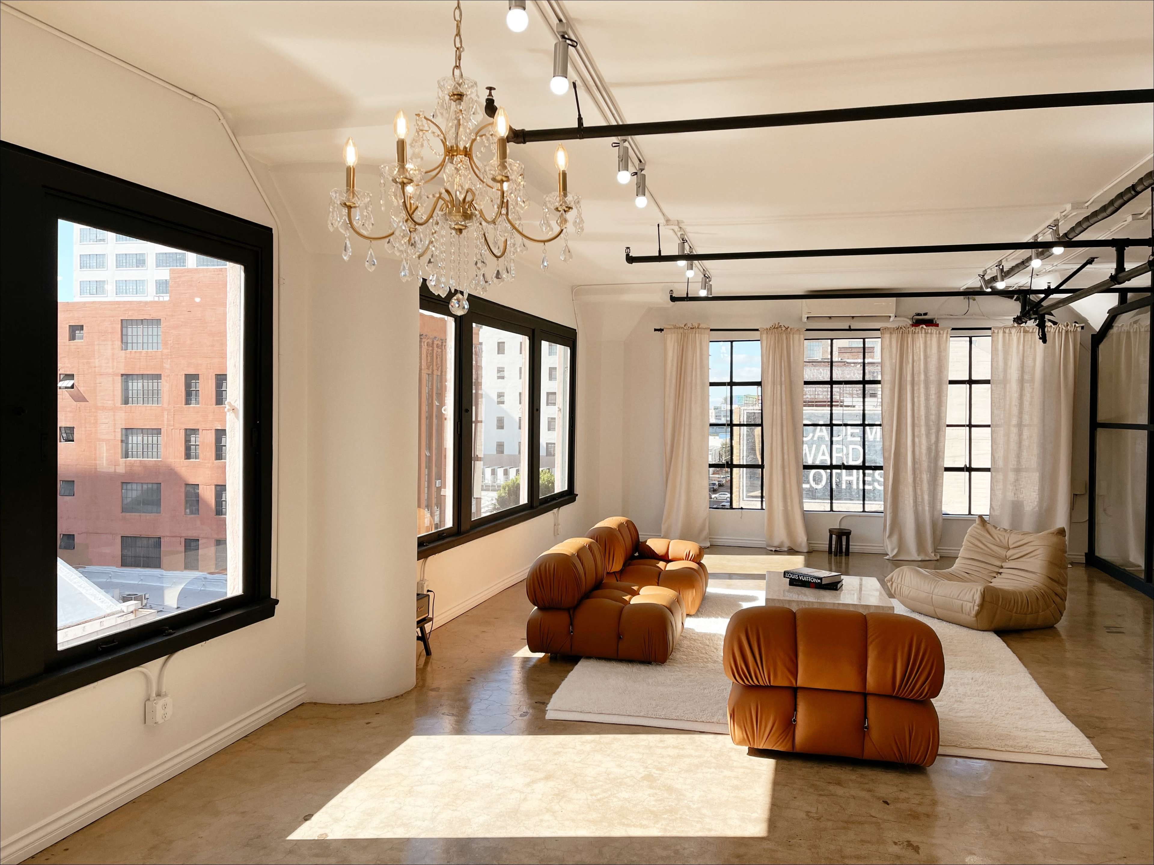 A modern, minimalist living space with large windows, a chandelier, and contemporary furniture arranged around a light-colored rug.