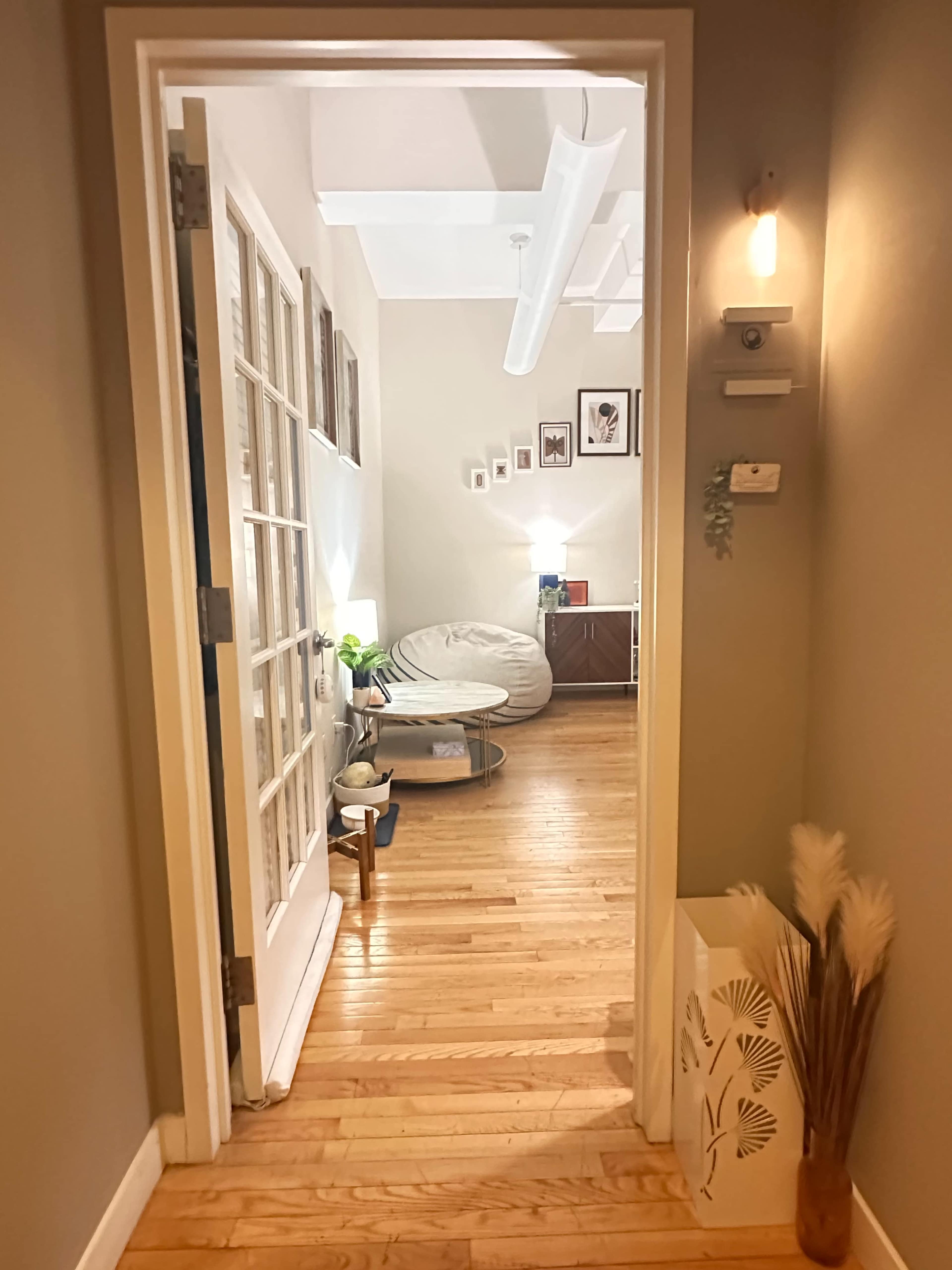 A well-lit hallway leads to a cozy living area featuring a large bean bag chair and decorative wall art.