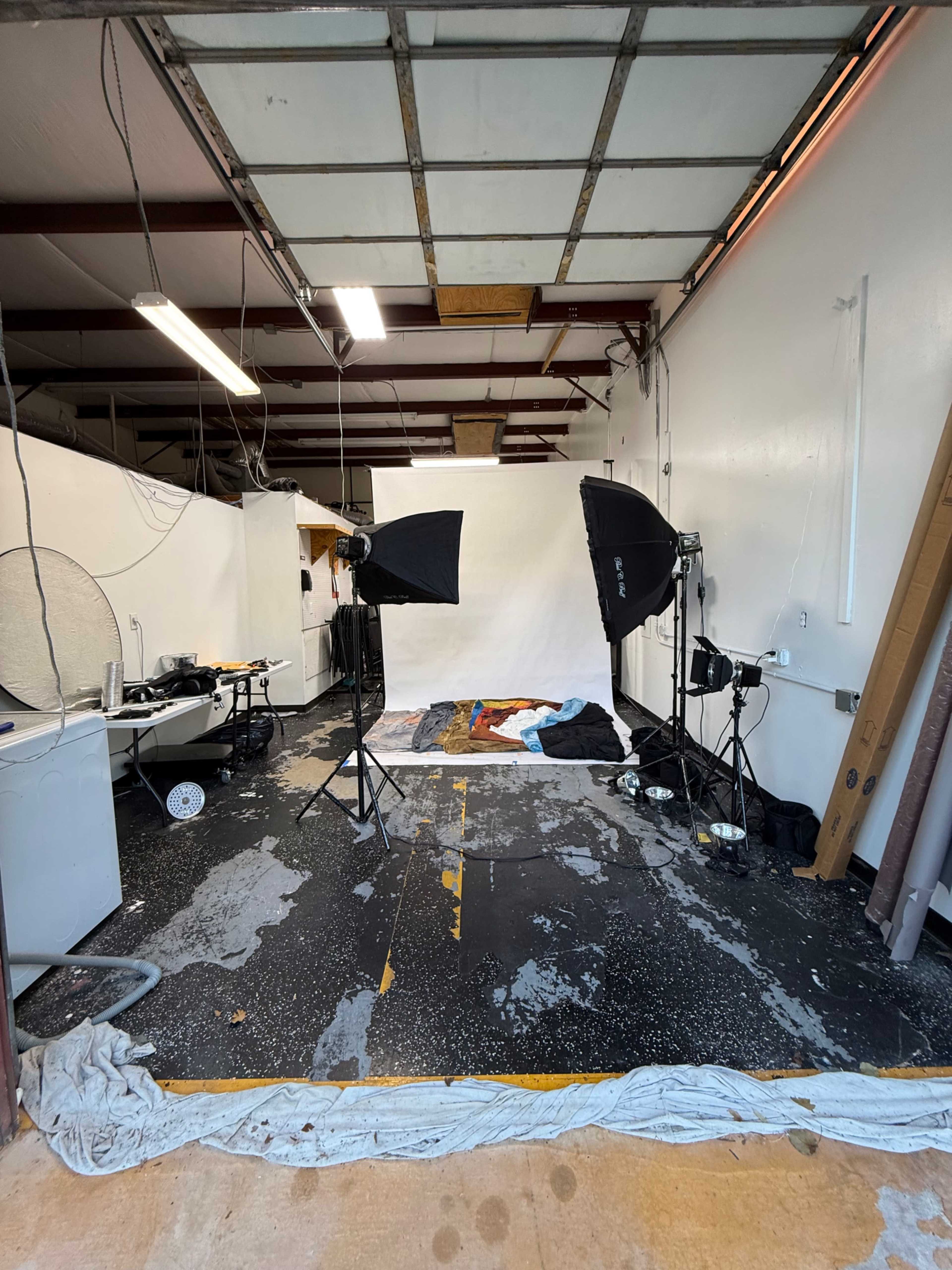 The image shows a photography studio with various lighting equipment, a backdrop, and a cluttered floor in a partially finished space.