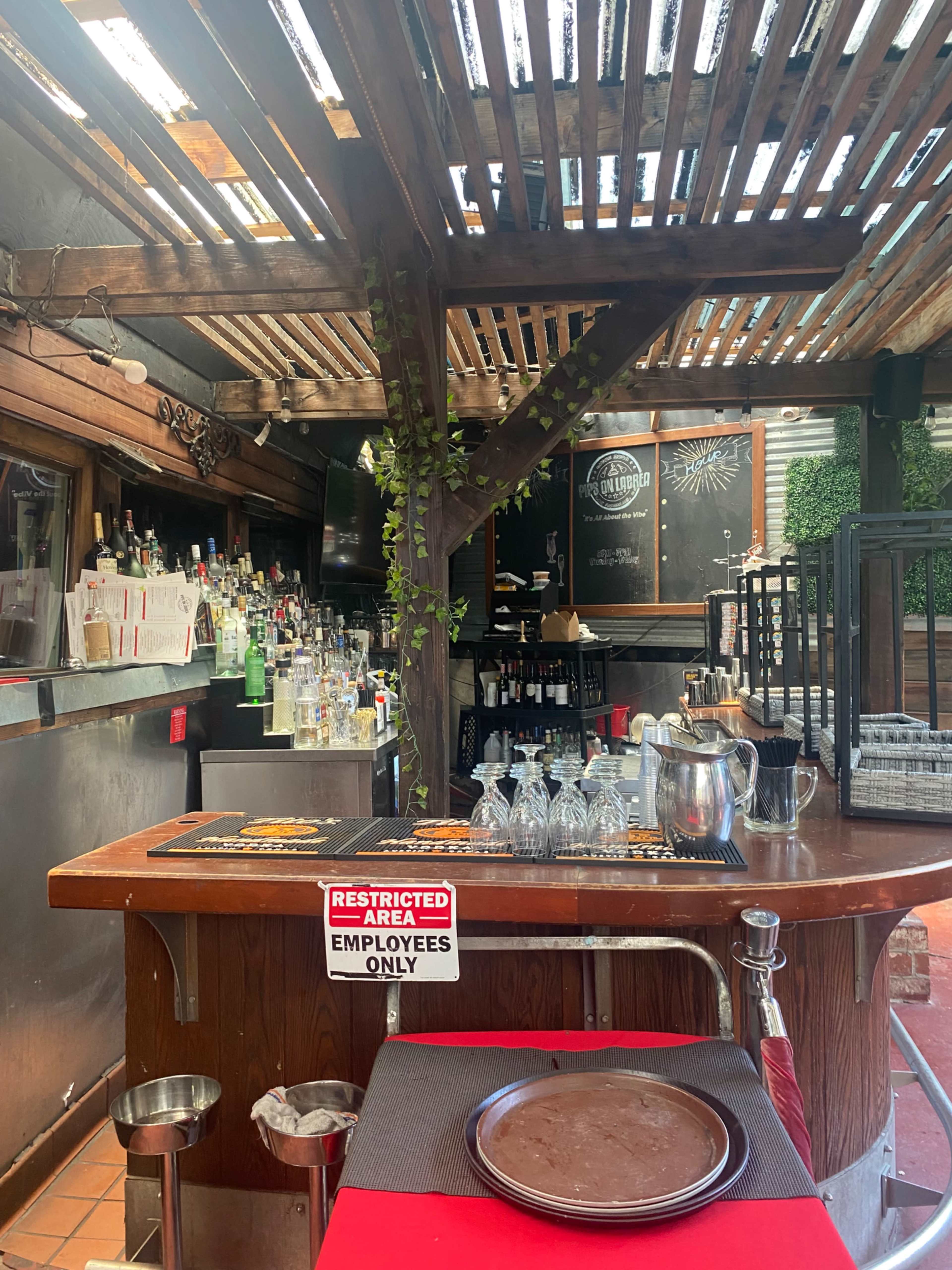 The image shows a bar area in a restaurant with a wooden structure, shelves filled with bottles, and a sign stating "RESTRICTED AREA EMPLOYEES ONLY."