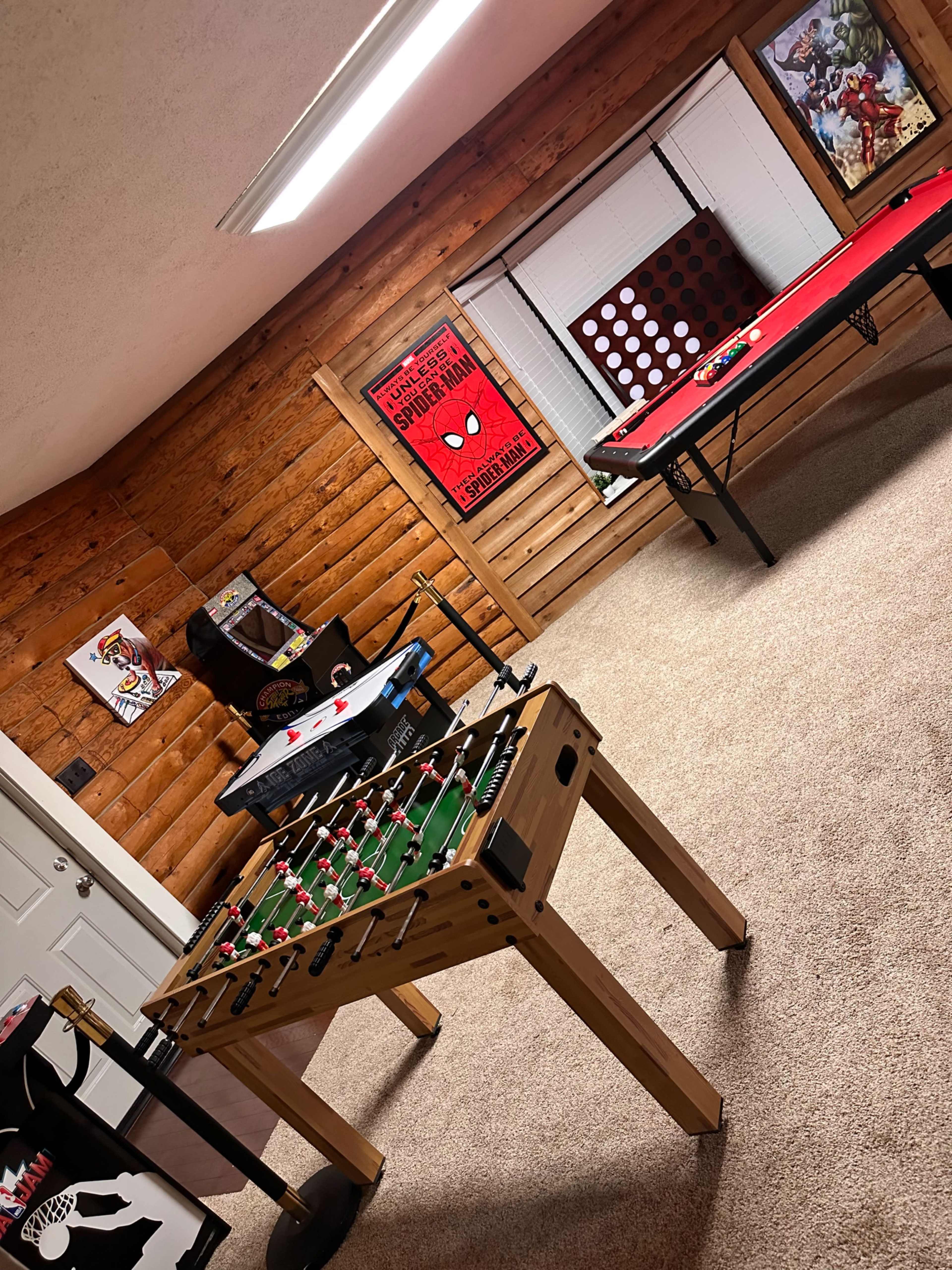 A game room with a foosball table, a poker table, and various wall decorations in a log cabin-style interior.