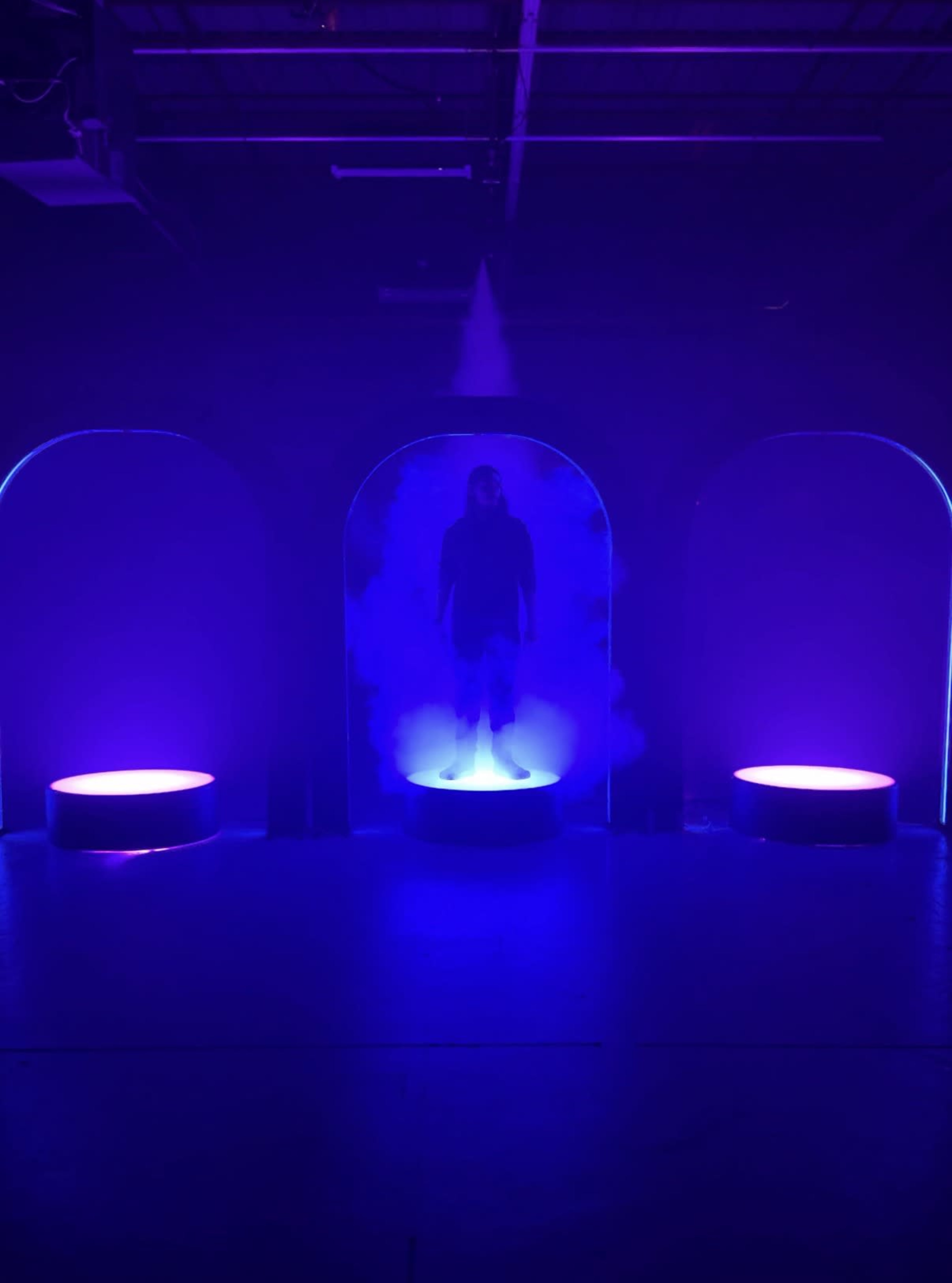 A person stands on a platform surrounded by purple lights and mist in a dark room.