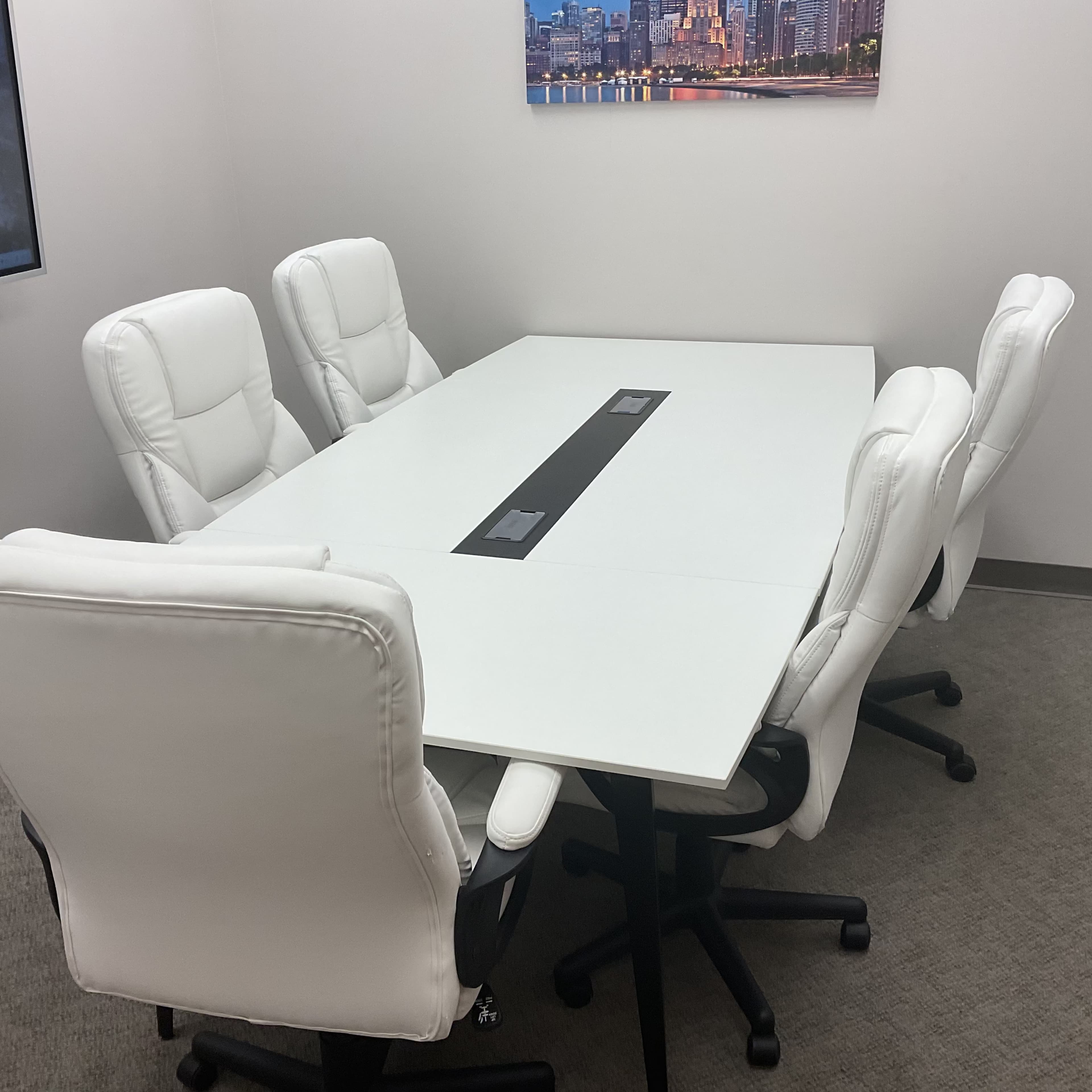 A modern conference room features a large white table surrounded by six white ergonomic chairs.