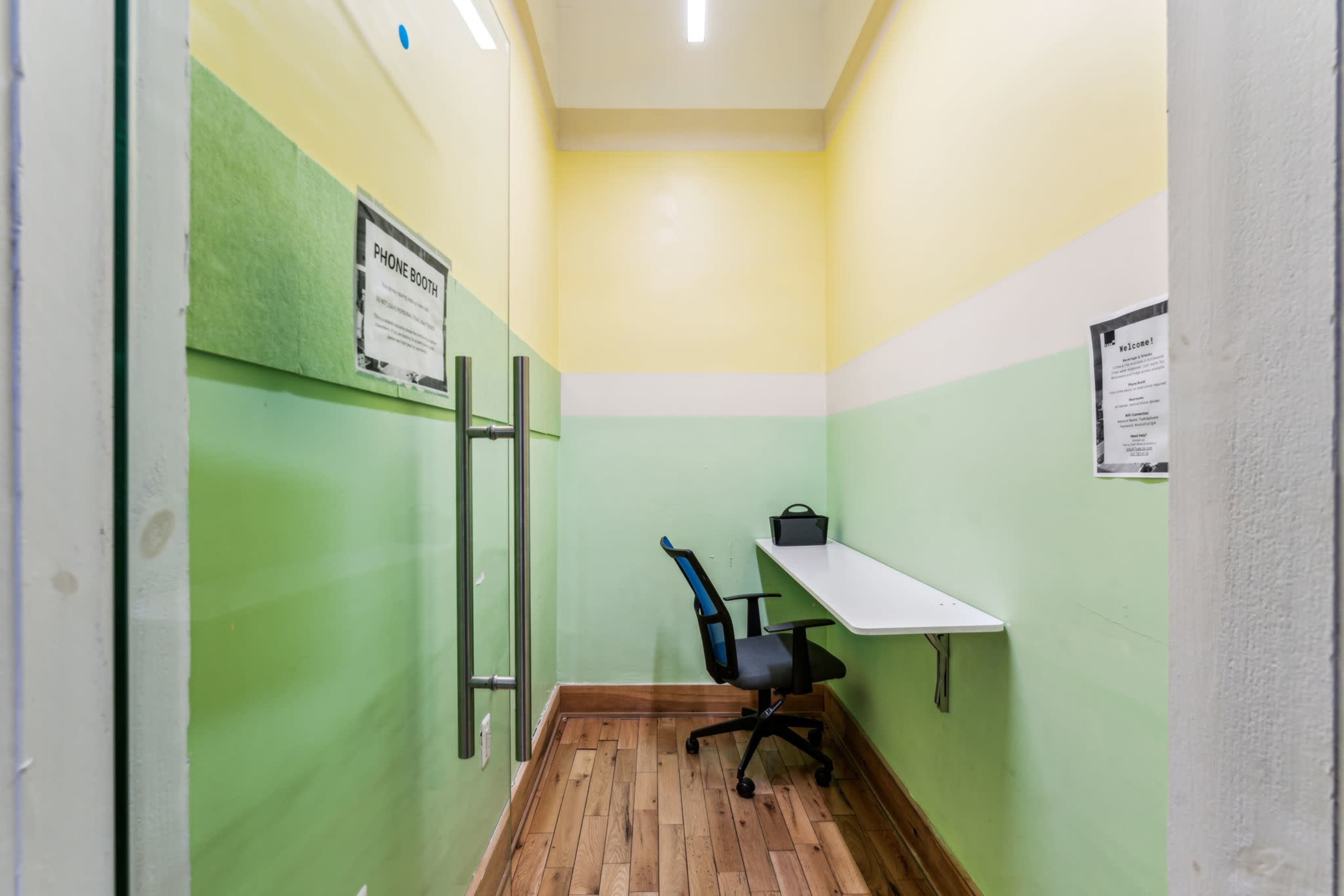 The image shows a small, brightly colored phone booth with a desk and a chair against one wall.