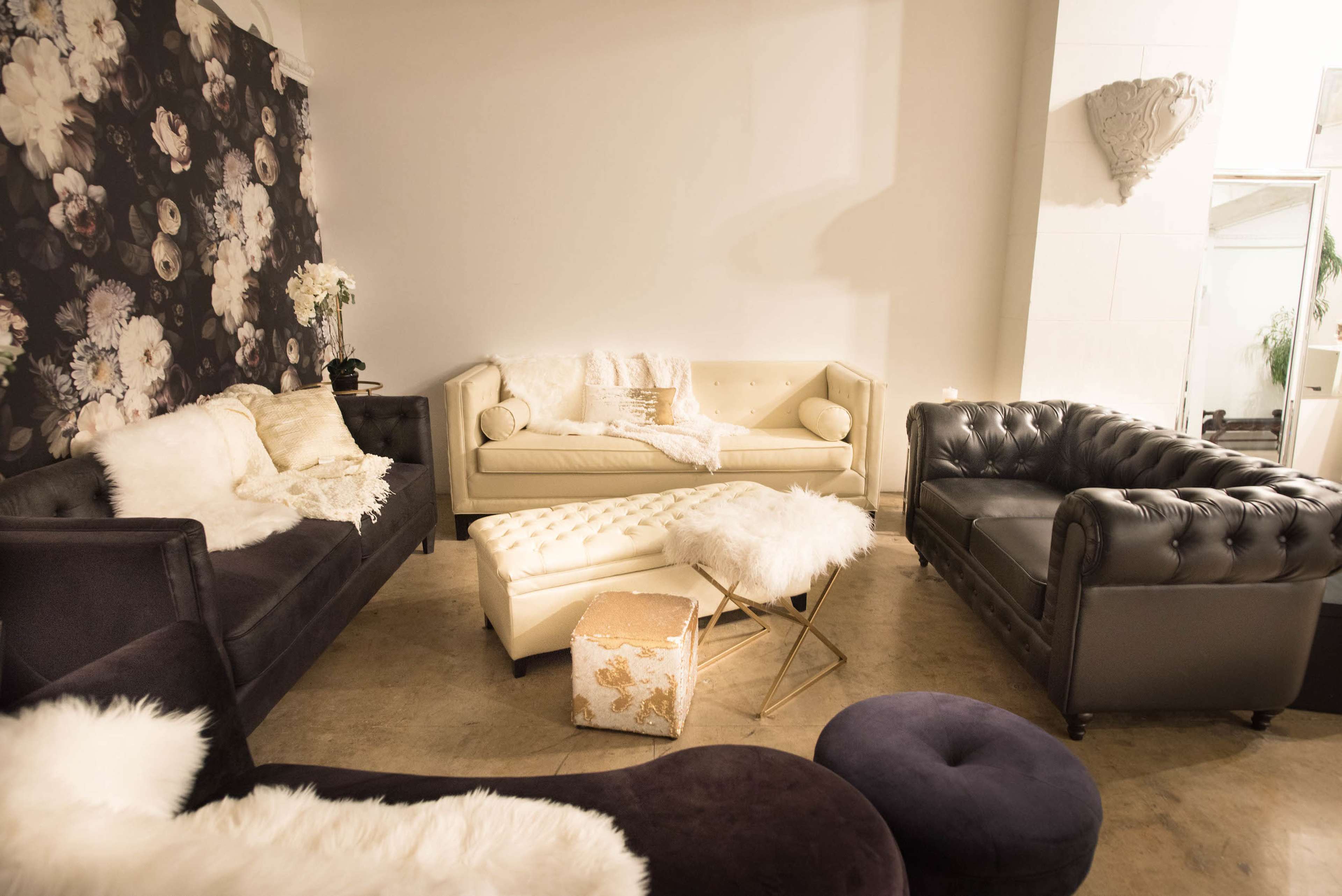 A seating area featuring several couches, a coffee table, and decorative pillows arranged in a stylish, modern setting with floral wallpaper.