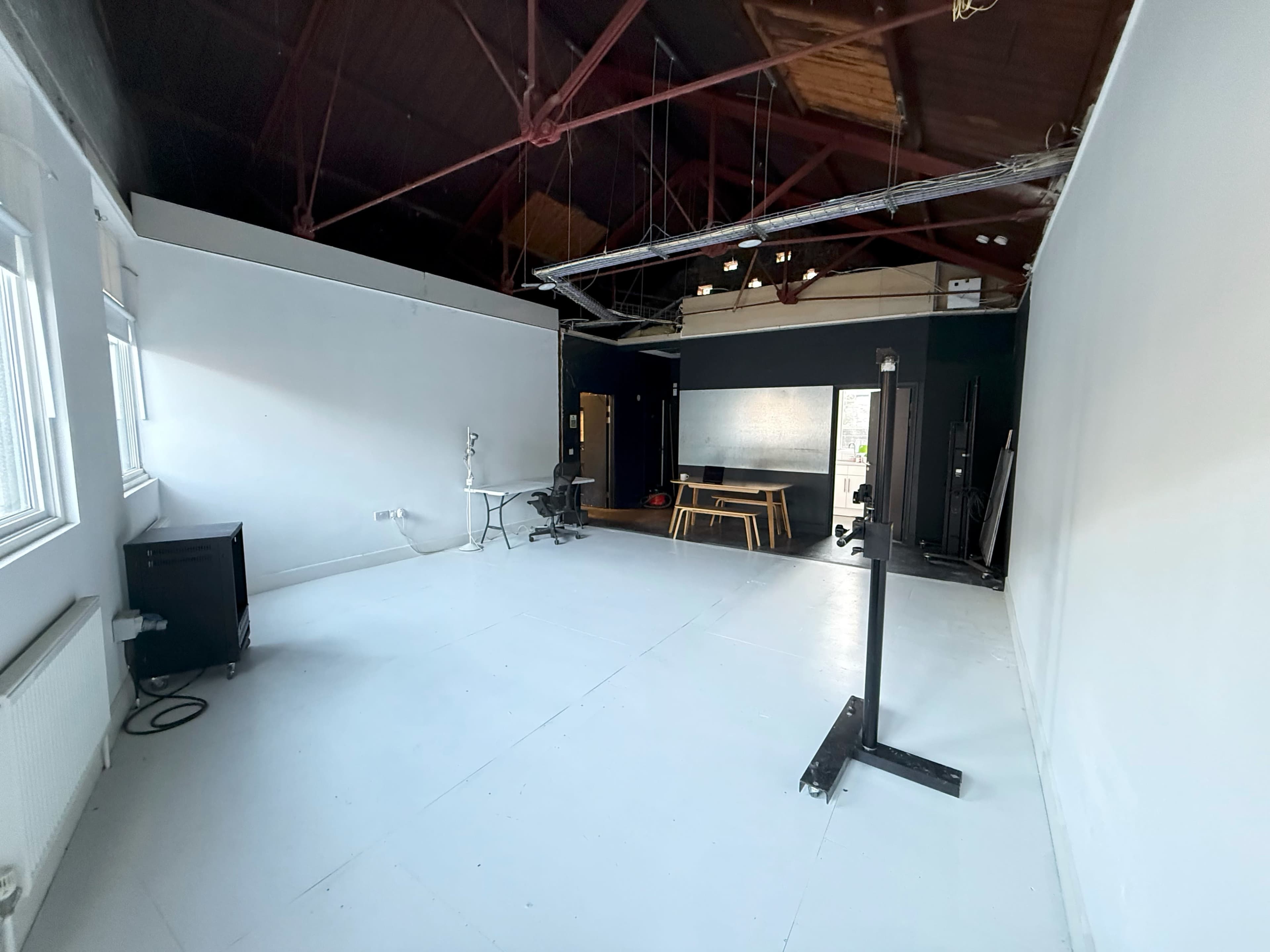 The image shows a spacious, empty studio with white walls, large windows, and a high ceiling.