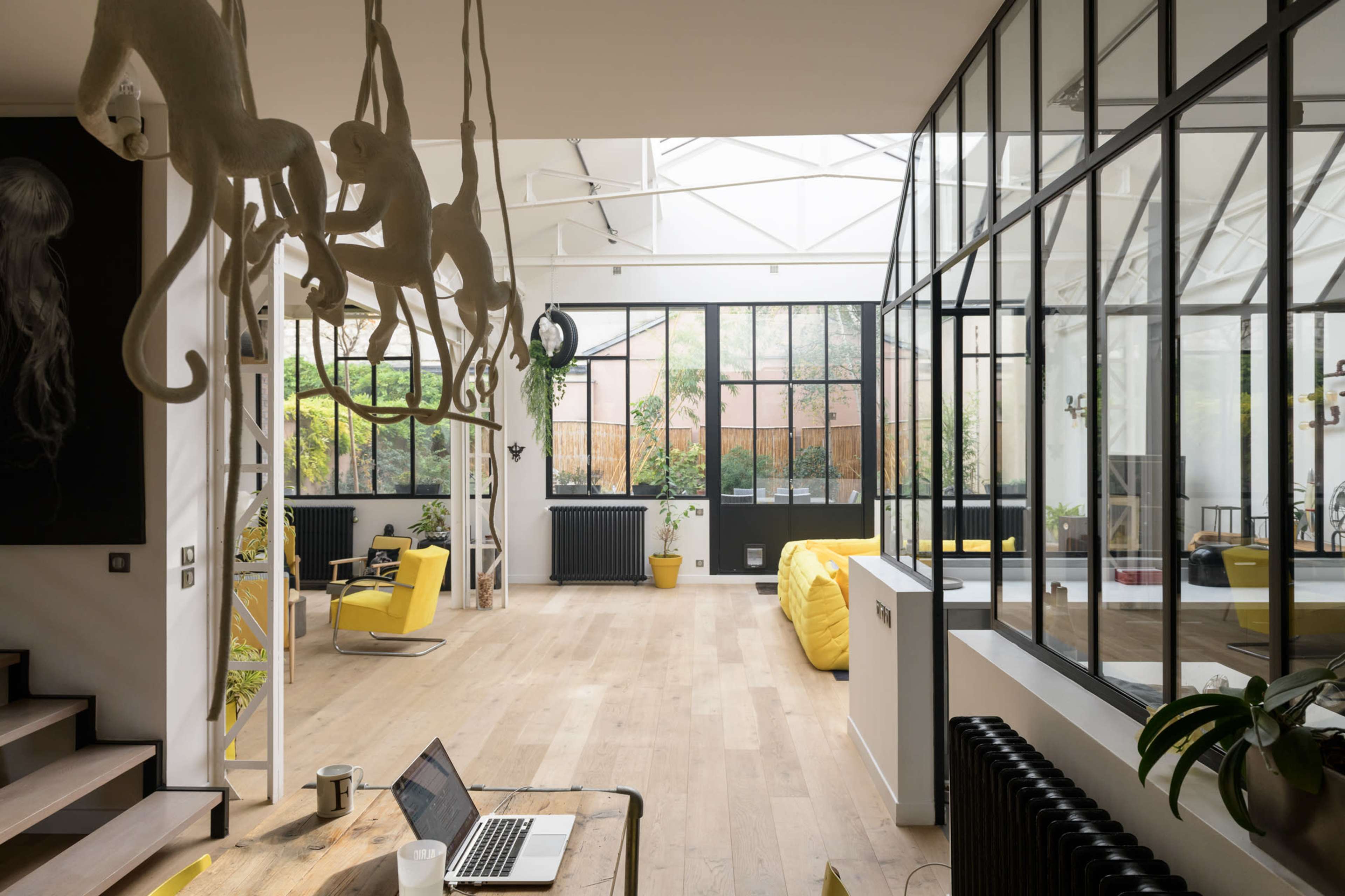 A spacious, modern open-plan interior featuring large windows, a wooden floor, and hanging monkey sculptures.