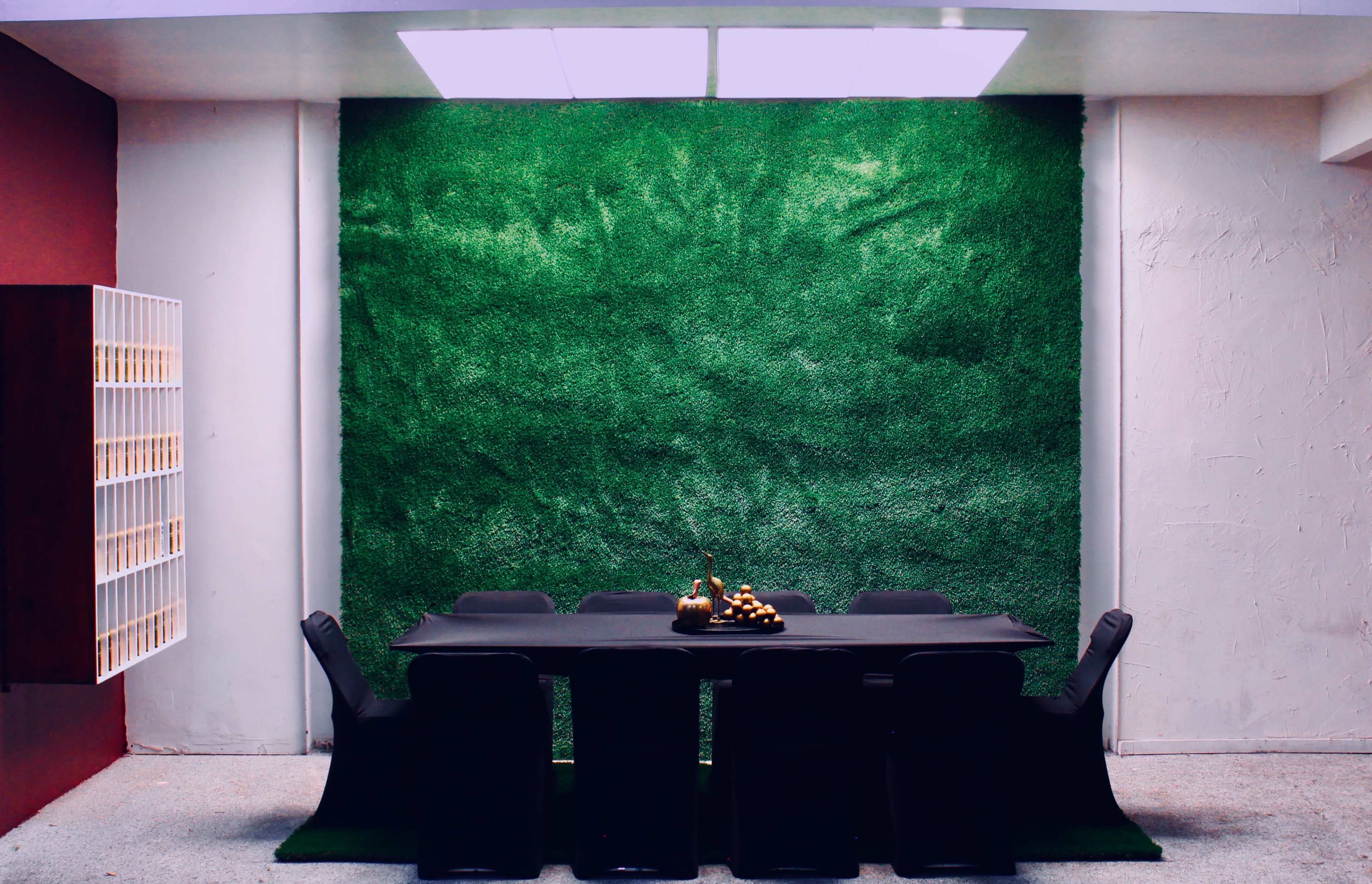A modern dining room features a black table surrounded by six chairs, set against a vibrant green grass wall.
