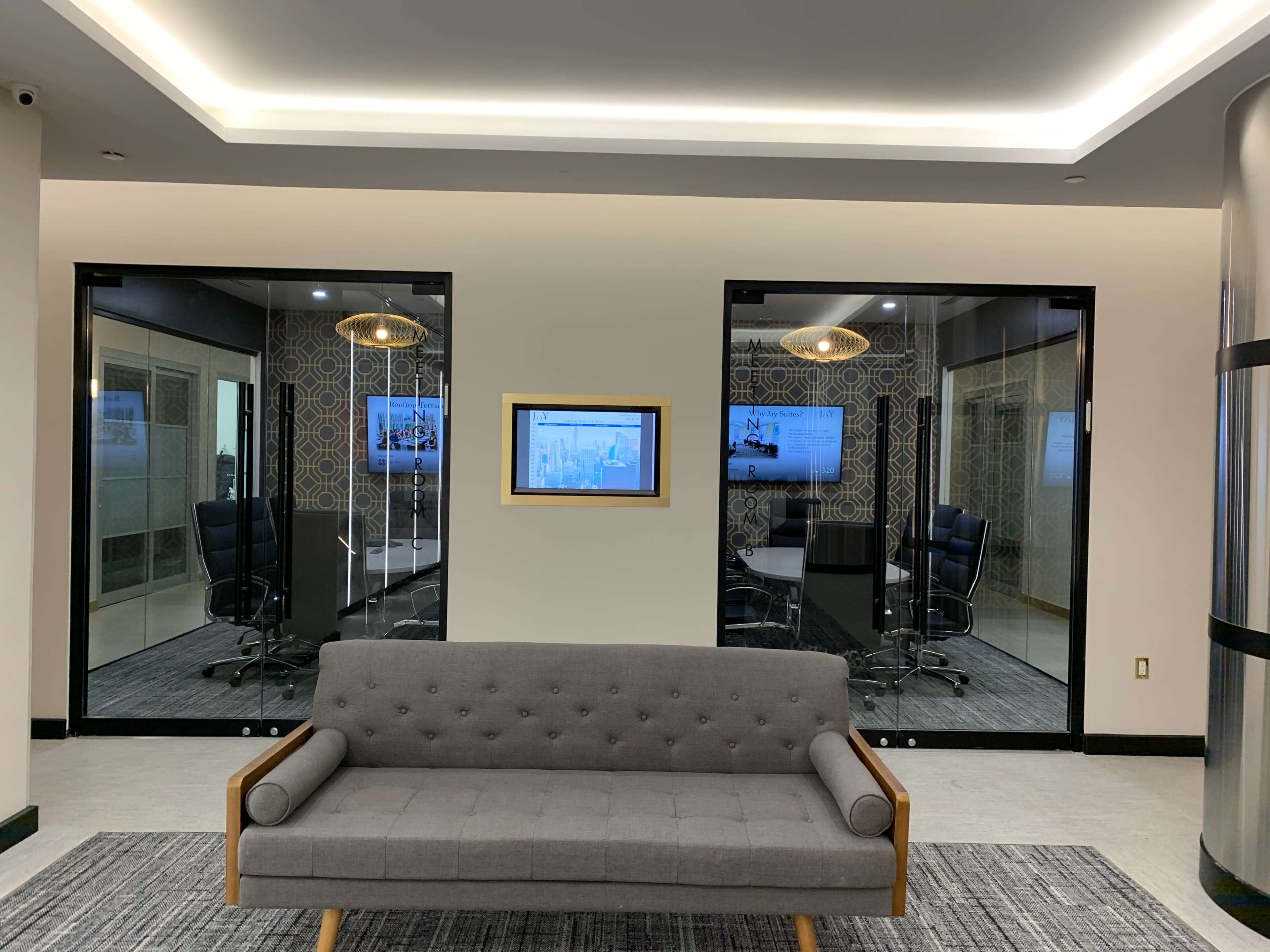 The image shows a modern office space with a gray sofa in the foreground and two glass-walled conference rooms visible in the background.