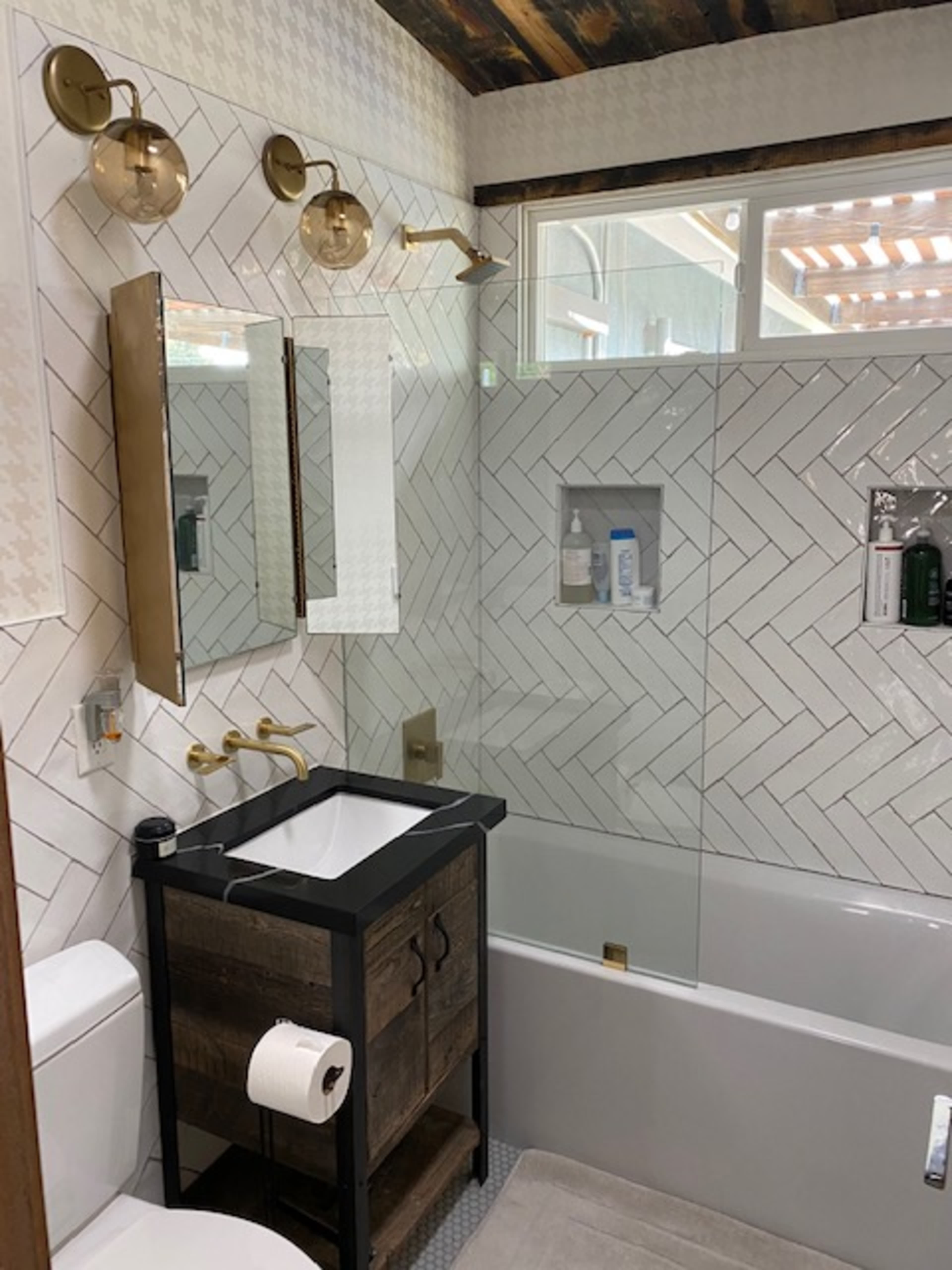 The bathroom features a tiled wall with herringbone patterns, a bathtub, a wooden vanity with a sink, and a large mirror.